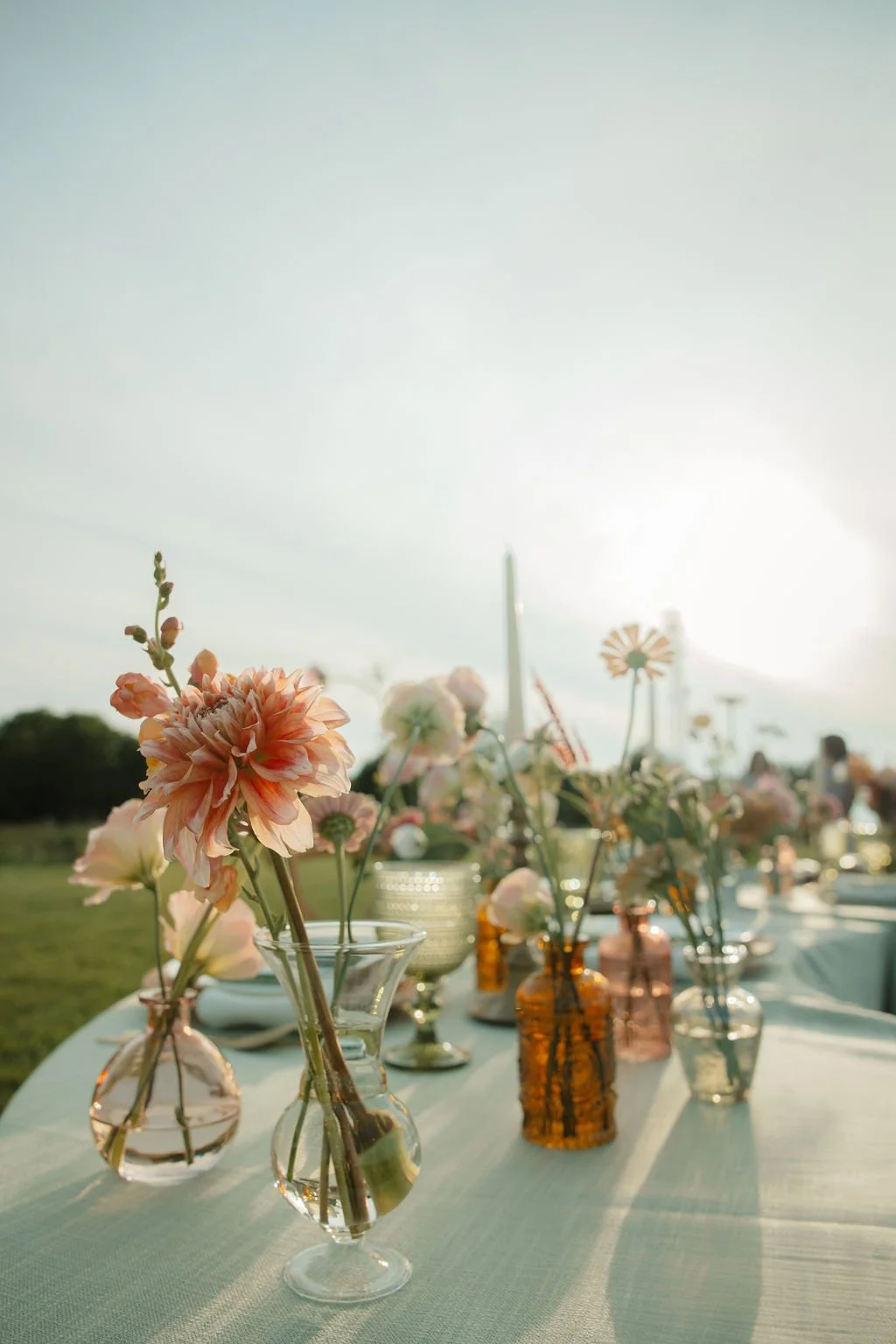 Vases with pink and peach flowers on a table outdoors during sunset.