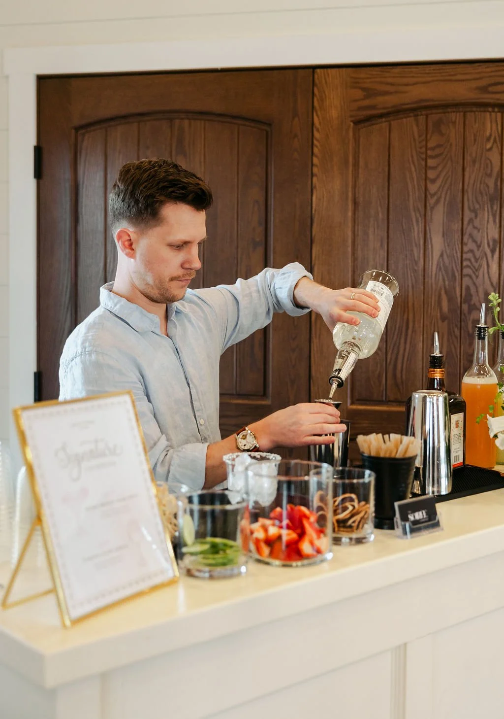 A bartender preparing a drink behind a bar with various bottles and garnishes.