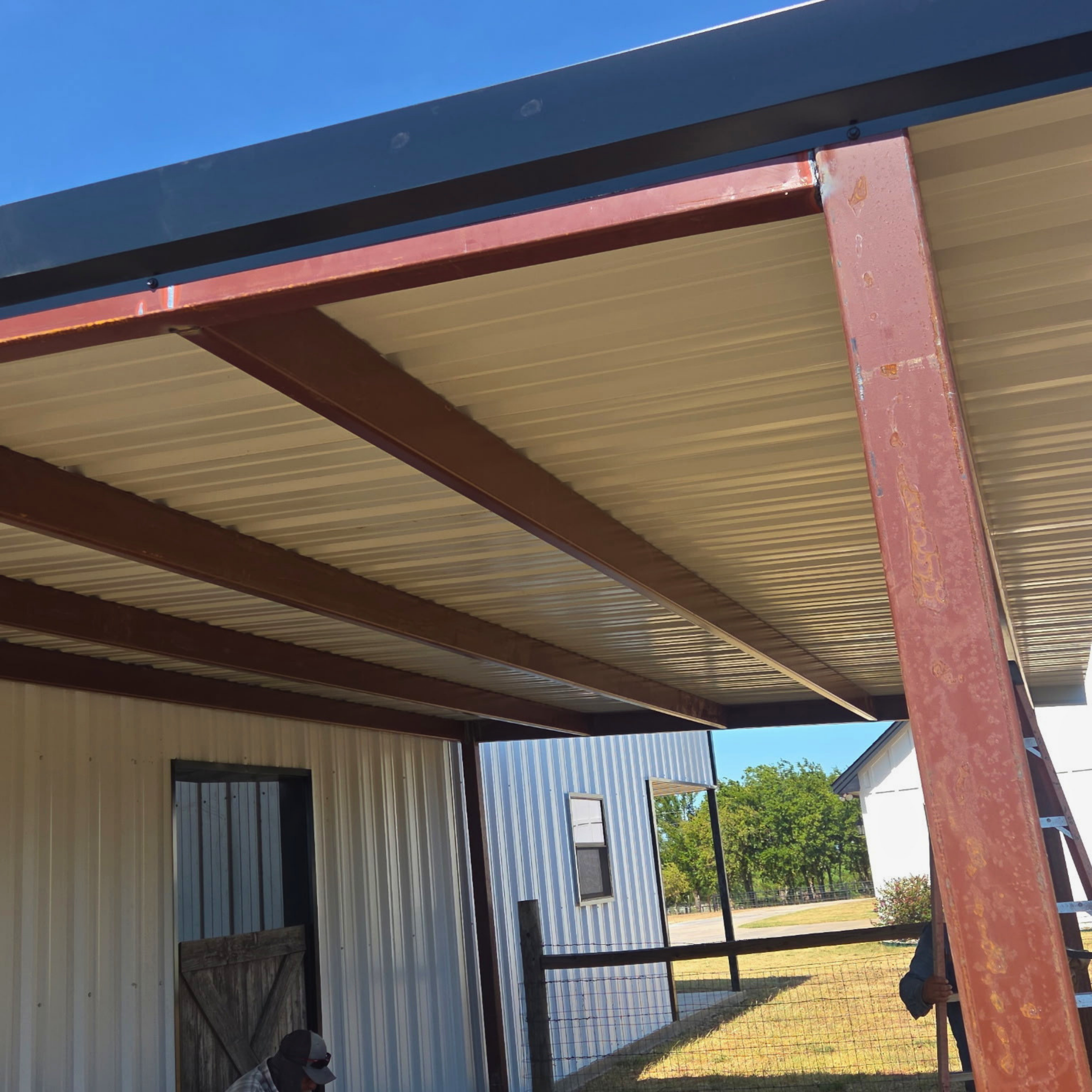 Cory of CMD General Construction under a custom metal awning,  with steel beams and a clear blue sky in the background.