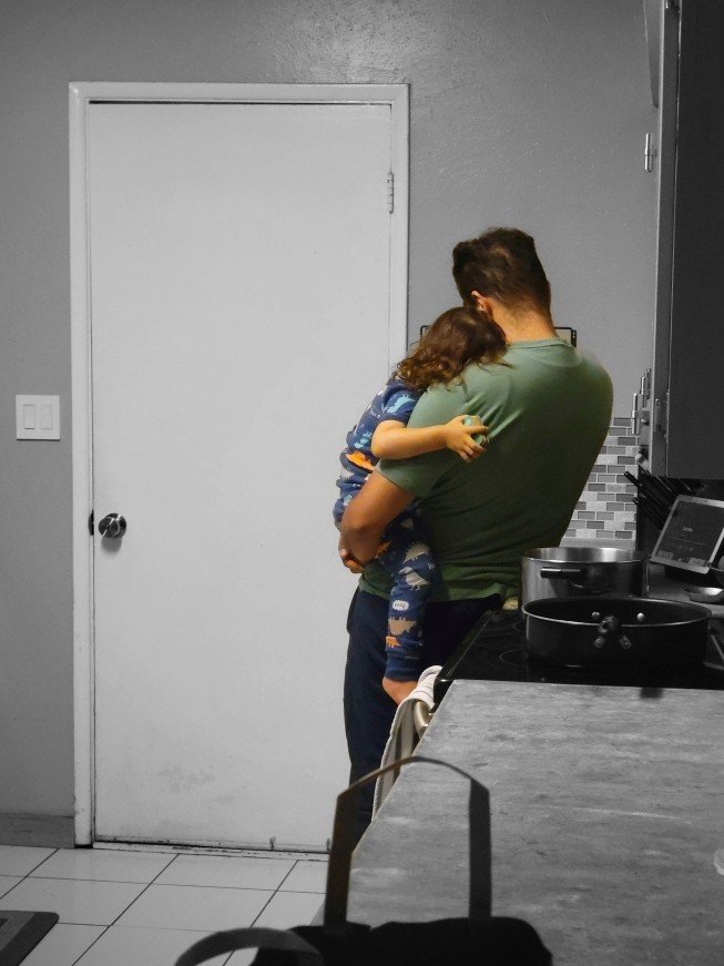 Dr. Correia holding his young son in his arms in a kitchen before bed, with a closed white door and part of a stove visible.