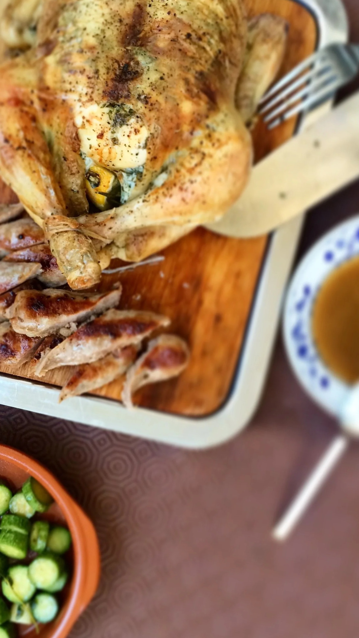 Roast chicken on a wooden serving board with sliced grilled chicken and a bowl of green peas with chopped cucumbers.