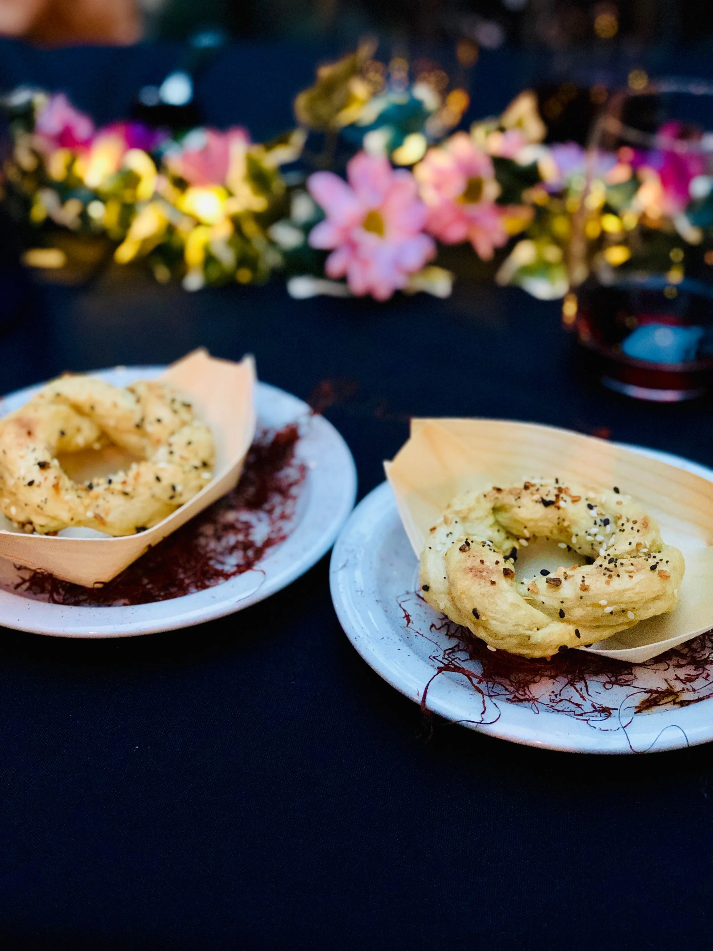 Close-up of two plates with ring-shaped foods, likely bagels or bread, topped with seasoning, on a dark surface.