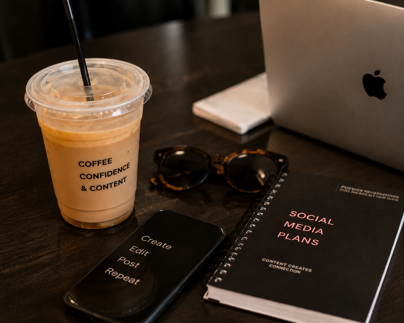 Creative workspace with iced coffee, laptop, smartphone, and social media planning materials.
