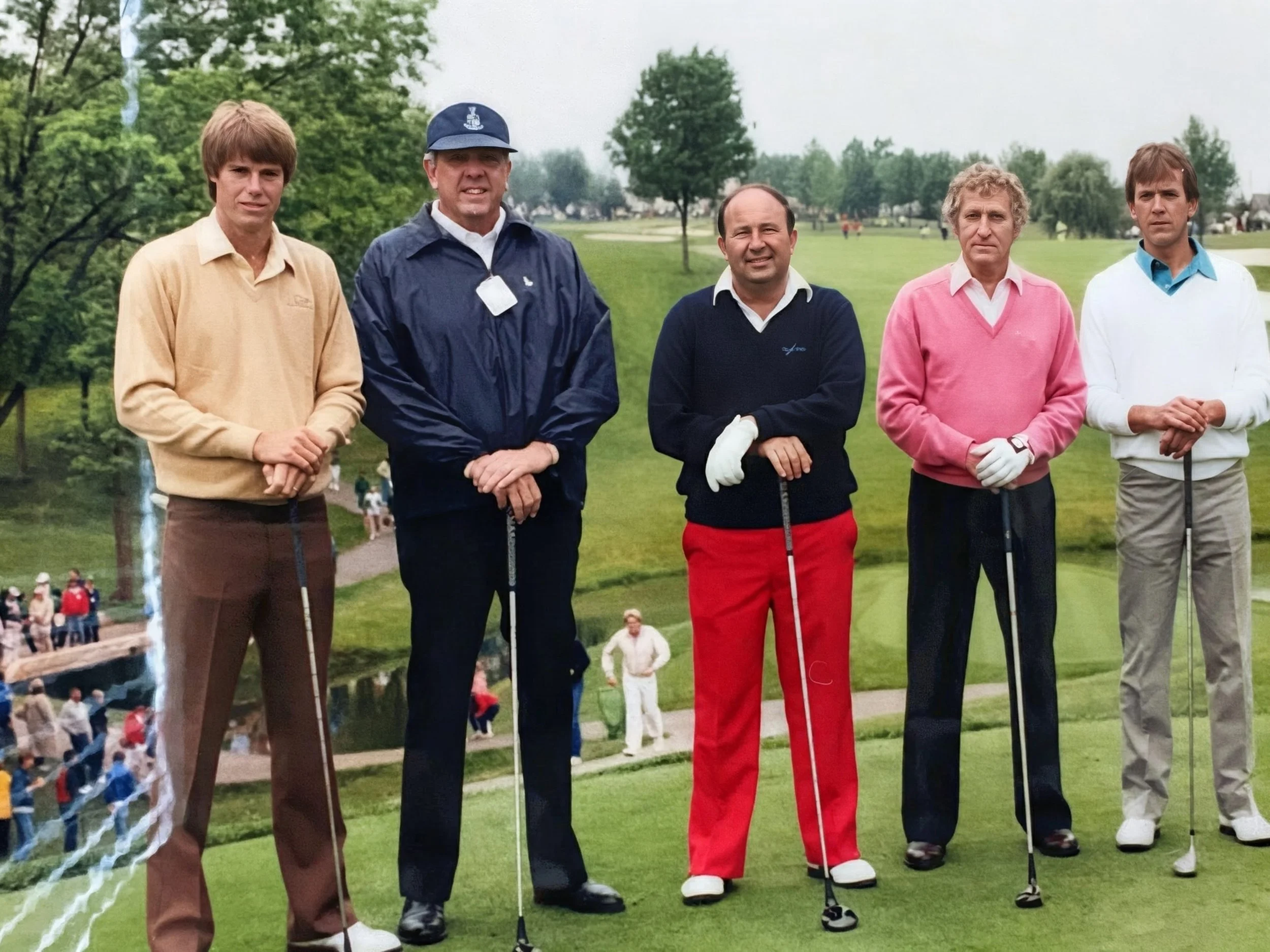 Five men standing on a golf course, holding golf clubs, dressed in golf attire, with trees and other people in the background.
