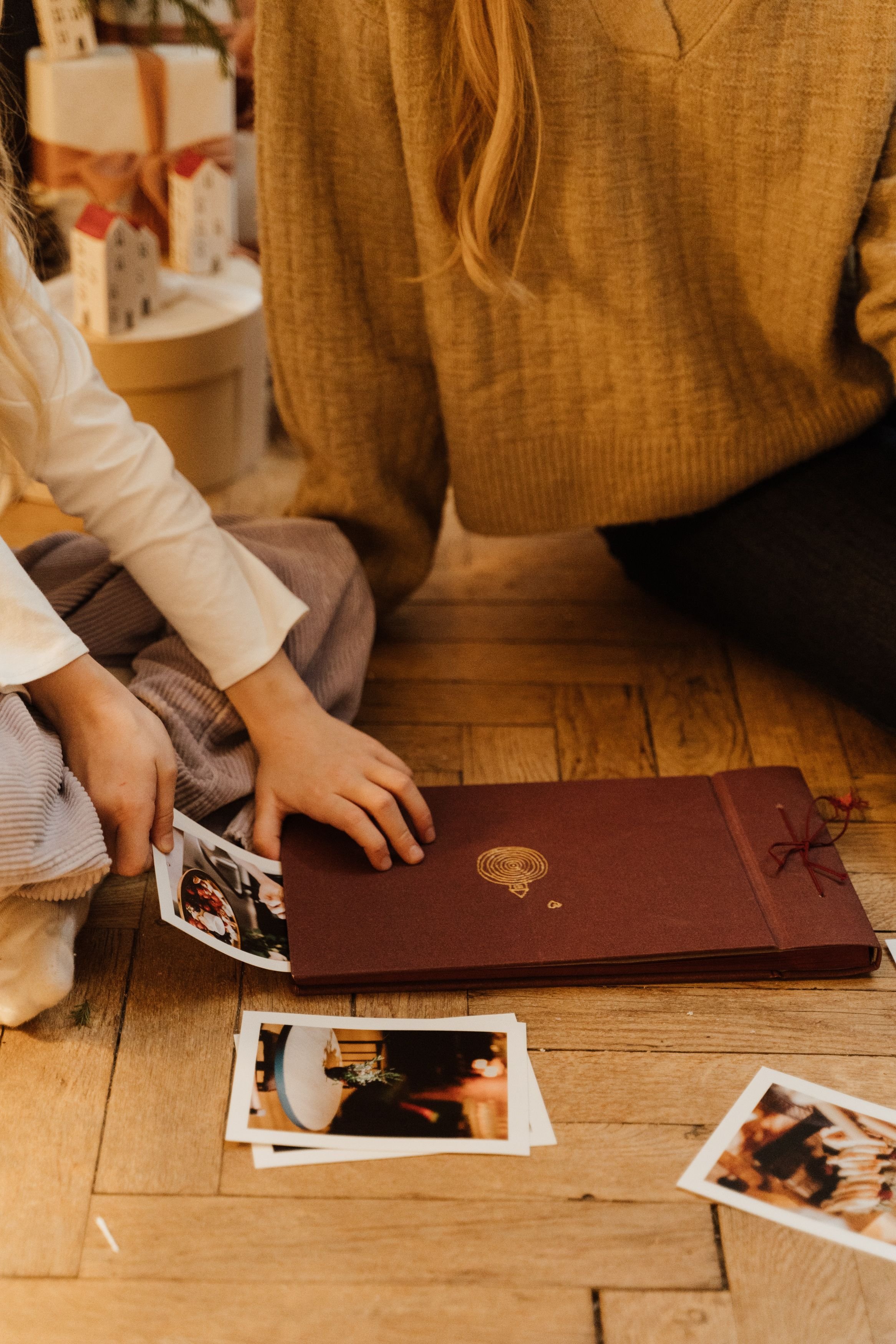 A mother and child sitting on a wooden floor organizing a photo album, creating family memories together.