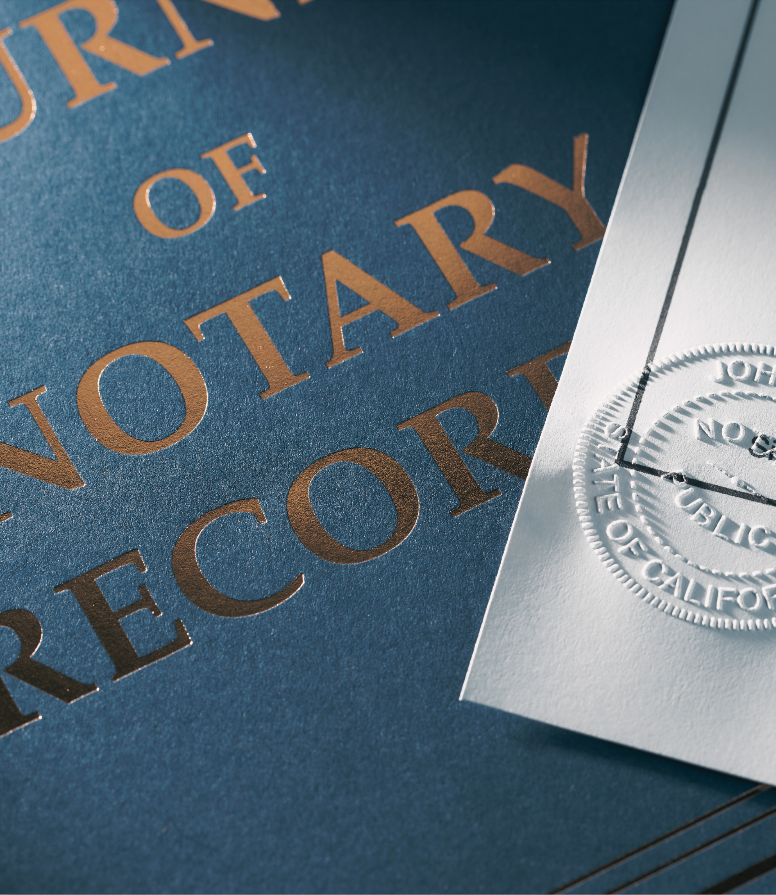 Close-up of a textured dark blue paper with metallic copper-colored embossed text and a white embossed seal.
