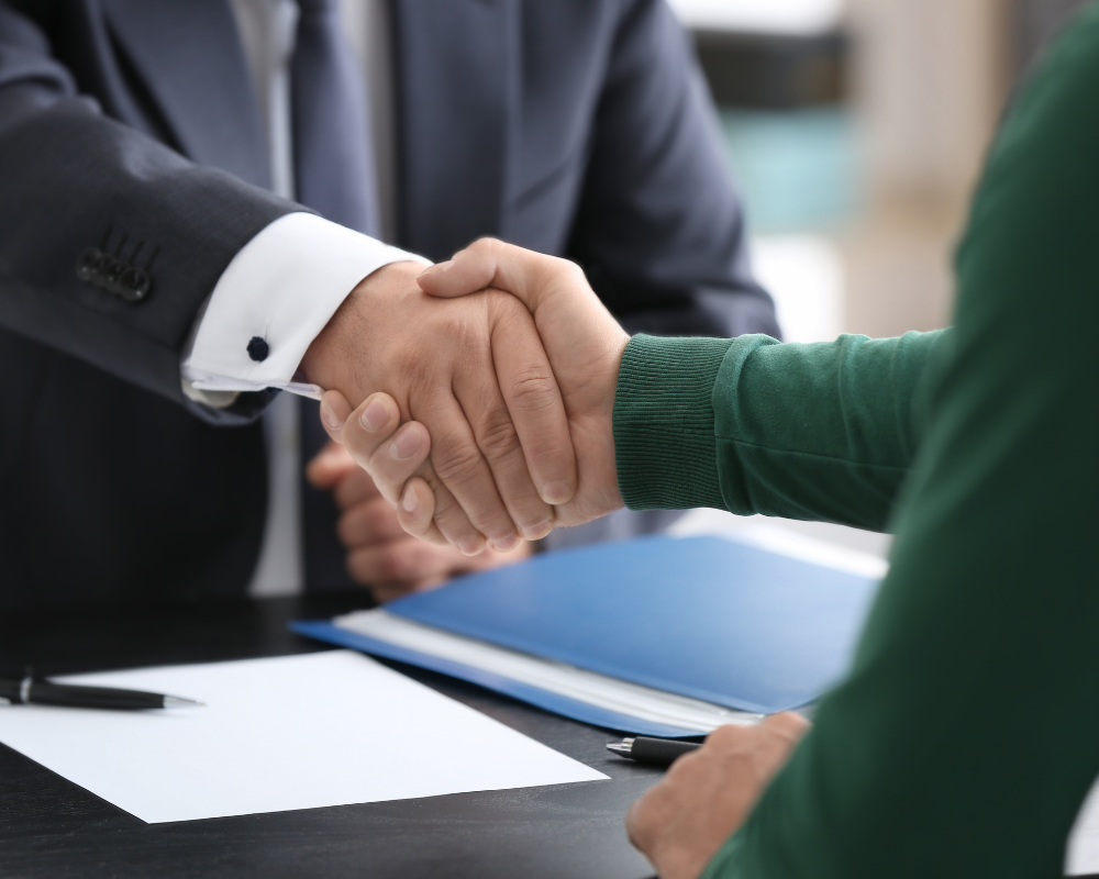Close-up of two people shaking hands over a desk, indicating a formal agreement or meeting.