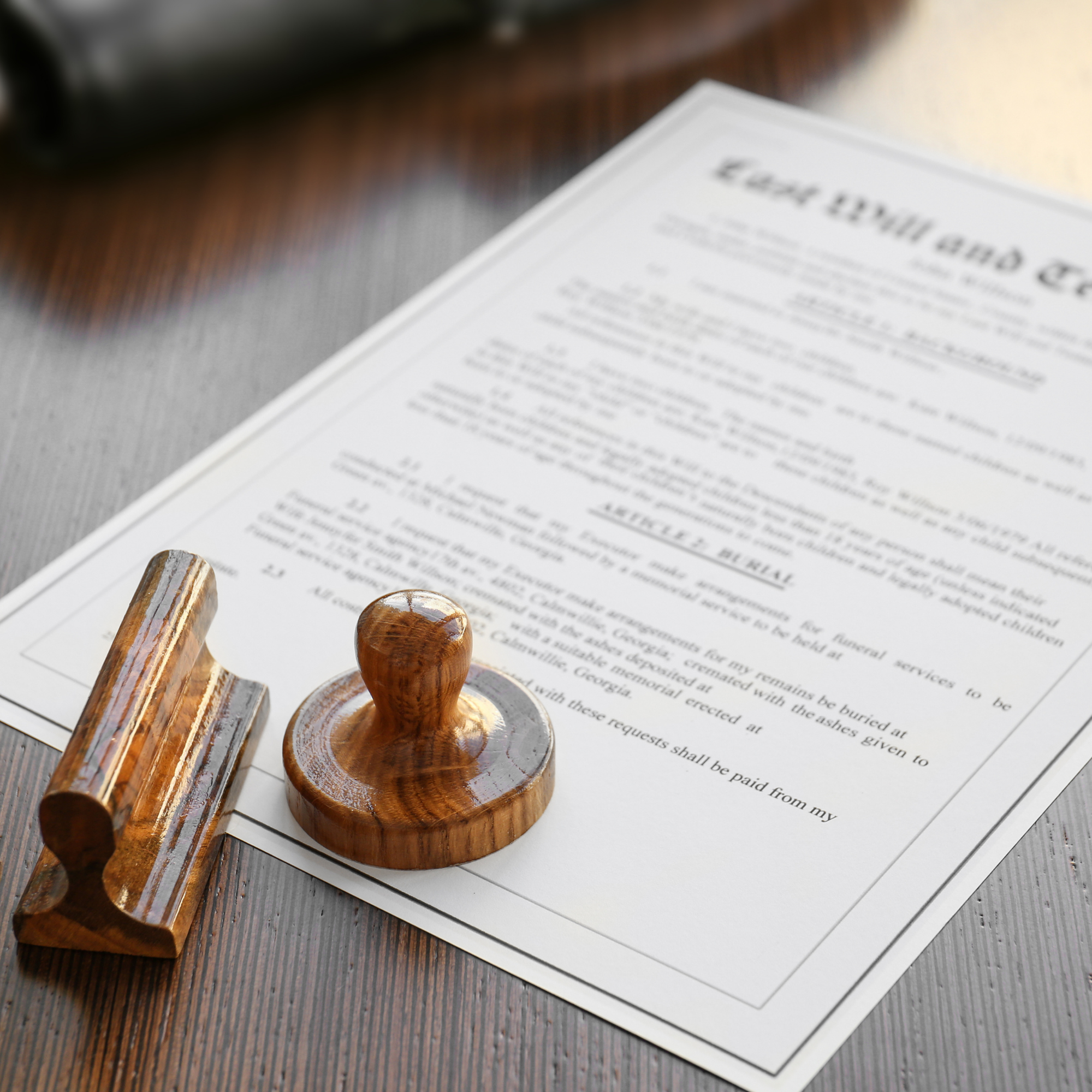 Close-up of a wooden stamp with a rounded handle placed on a document with blurred black uppercase text on white paper, resting on a wooden surface.