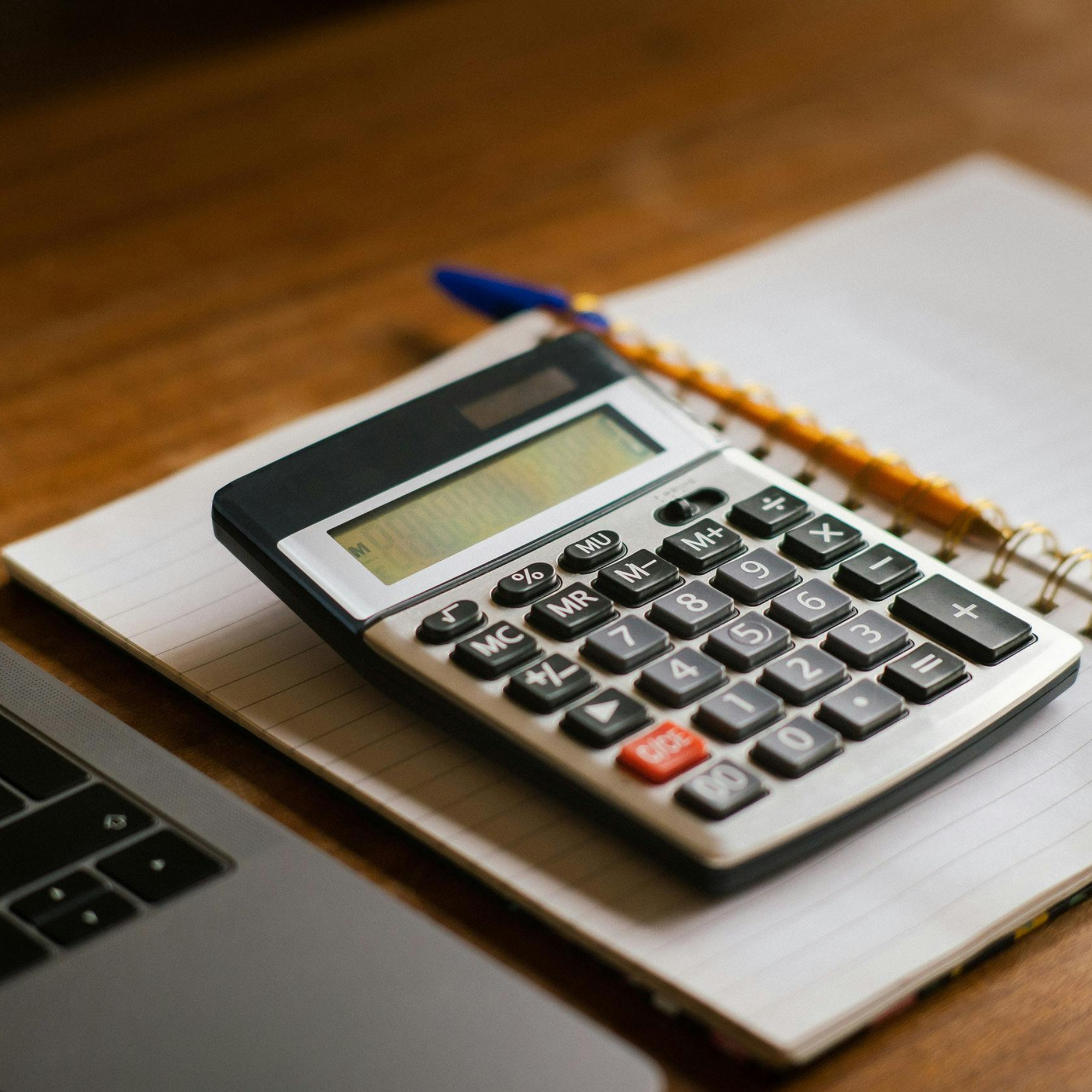 Close-up of a calculator resting on a spiral notebook with lined pages, on a wooden surface.