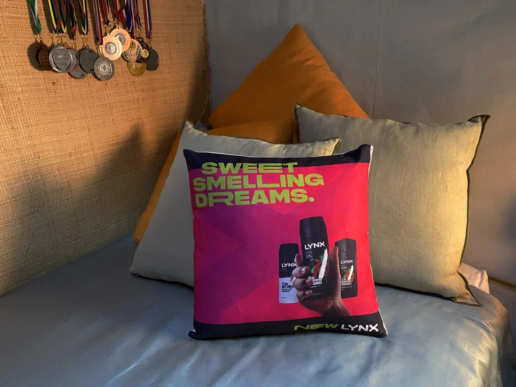 Almohadas y una almohadilla con un anuncio publicitario de productos Lynx, con el texto 'Sweet Smelling Dreams' y varias latas en la mano de una persona.