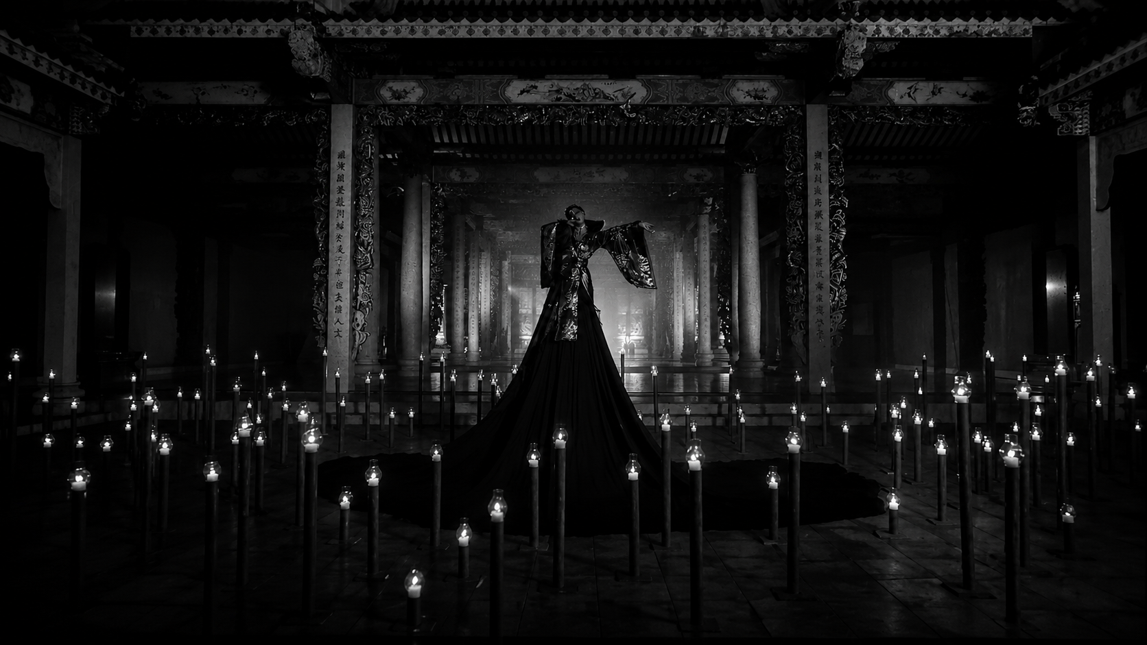 Figura en un escenario oscuro rodeada de velas, vestida con ropa elaborada y sobre una plataforma elevada en un templo o estructura tradicional con columnas decoradas.