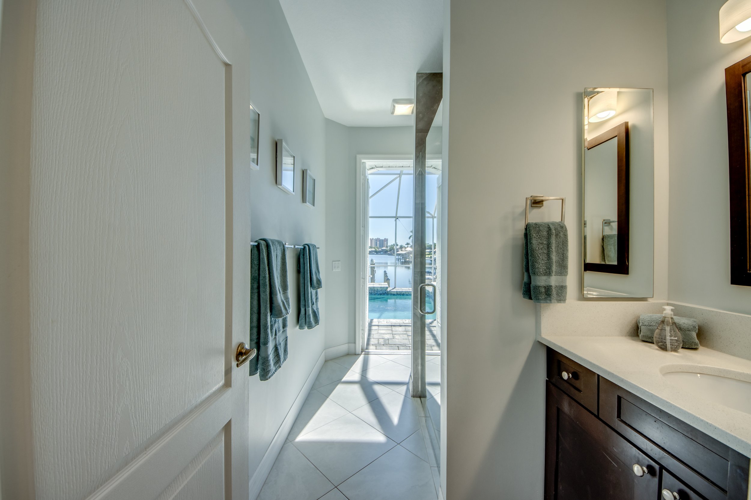 A bathroom with a vanity mirror, towels, and a view of a balcony with a pool outside and city skyline in the distance.
