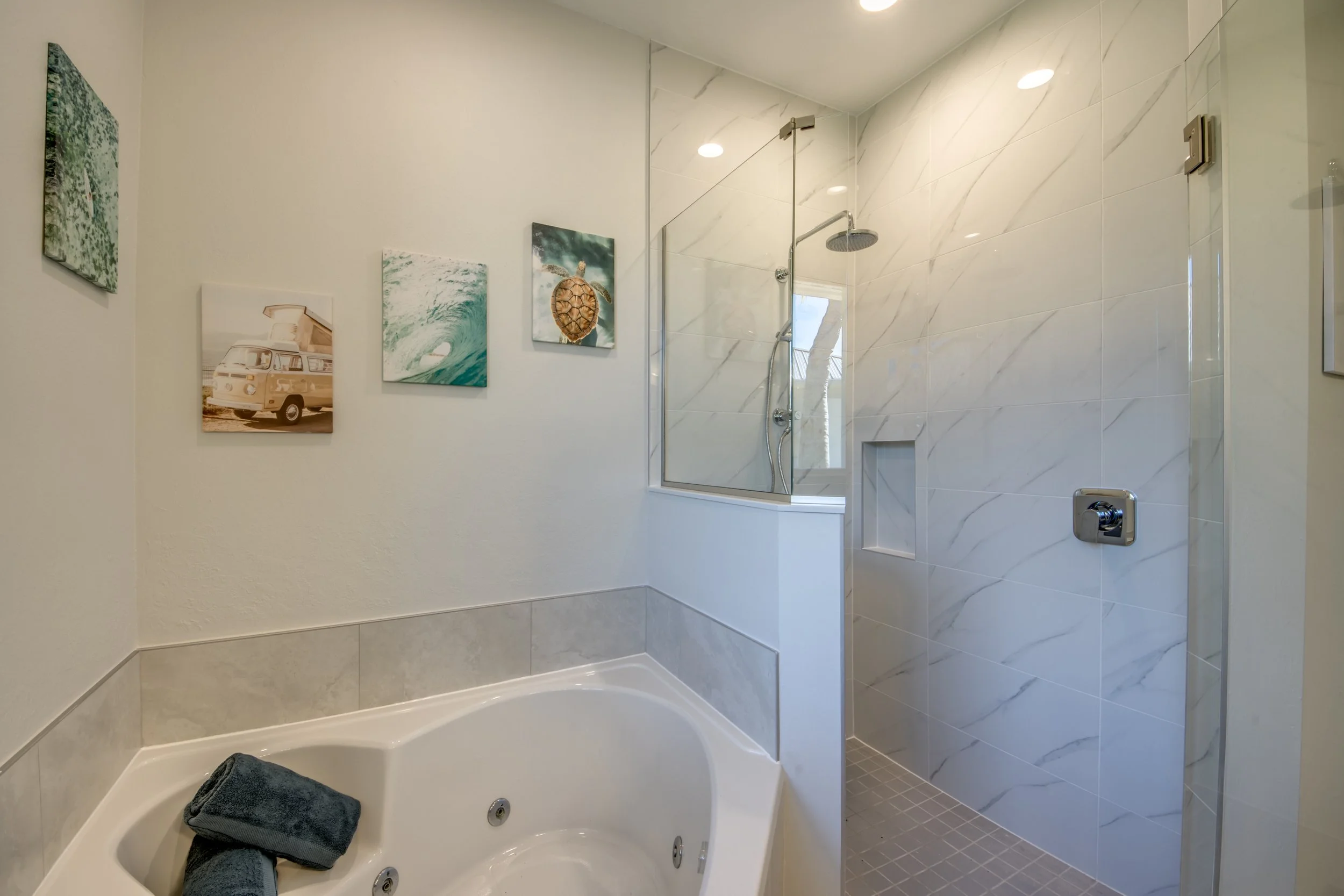 Bathroom with a jacuzzi tub, a walk-in shower with marble tiles, and framed ocean-themed artwork on the wall.