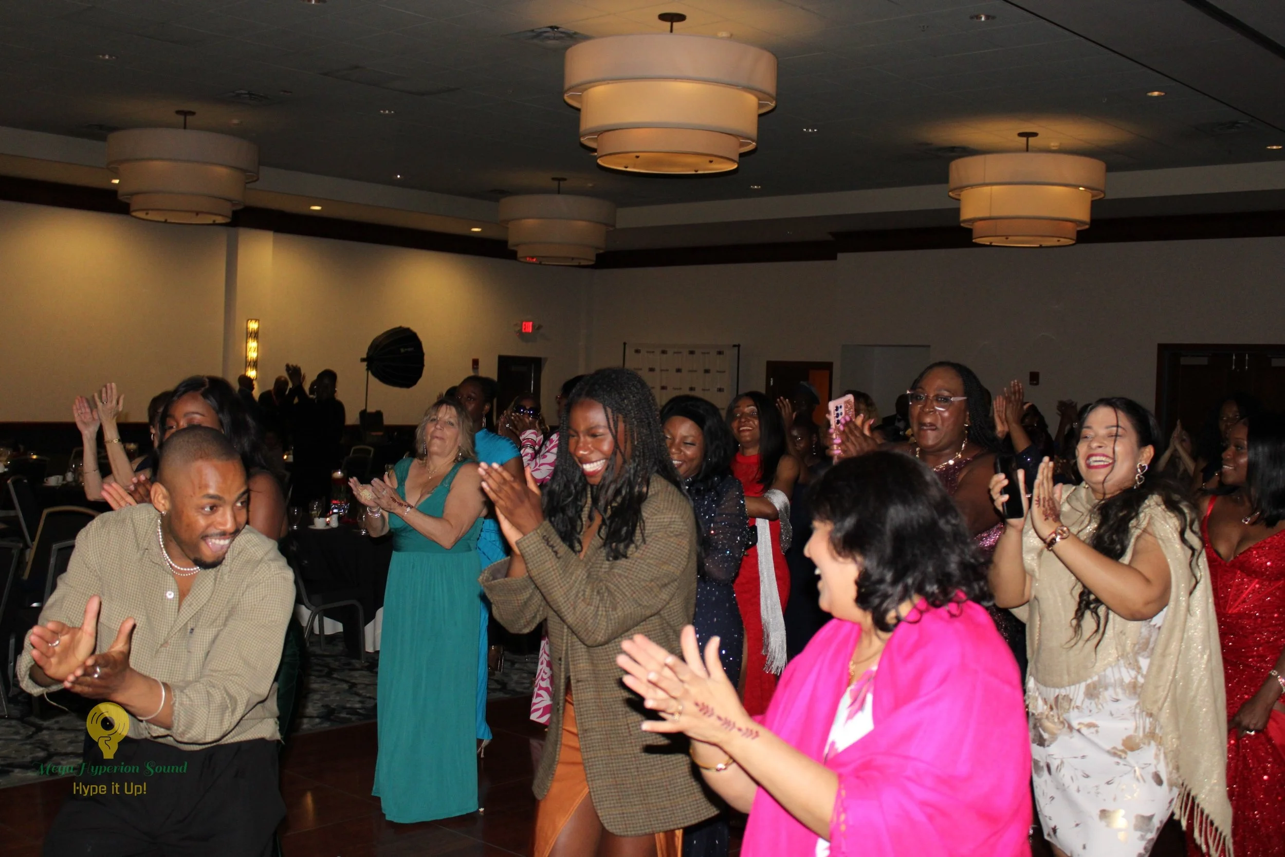 People dancing and clapping at a celebration event in a large room with ceiling lights.