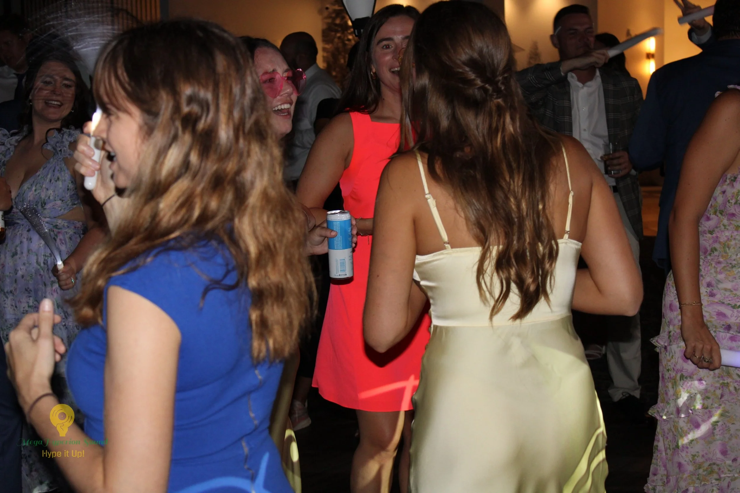 People smiling and chatting at an indoor social gathering, some holding drinks, with warm lighting and casual attire.