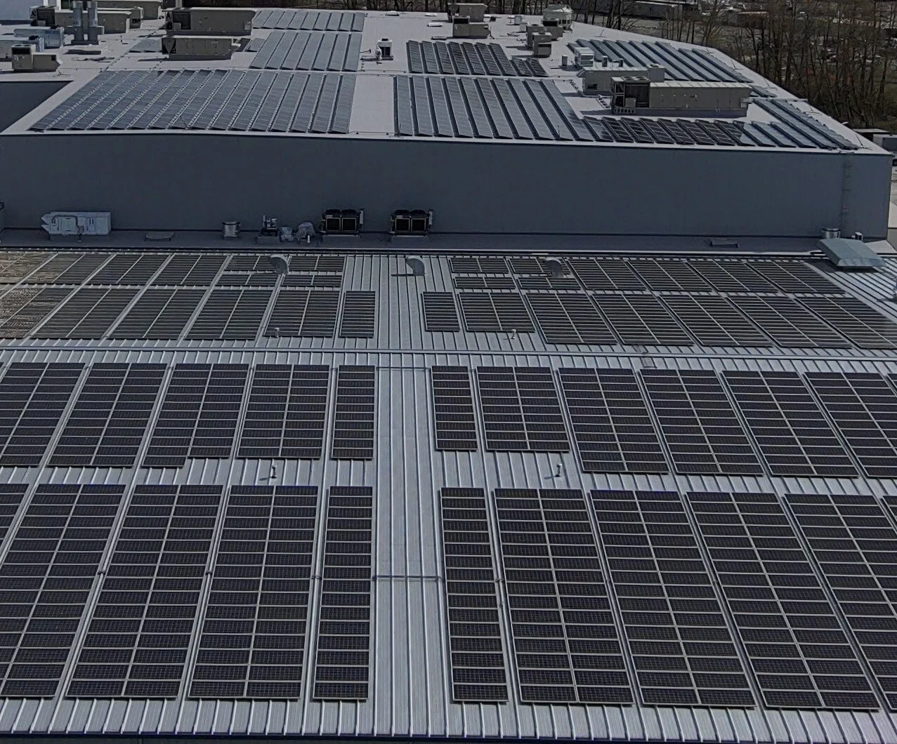 A rooftop covered with numerous solar panels installed in rows, with some HVAC units and vents visible.
