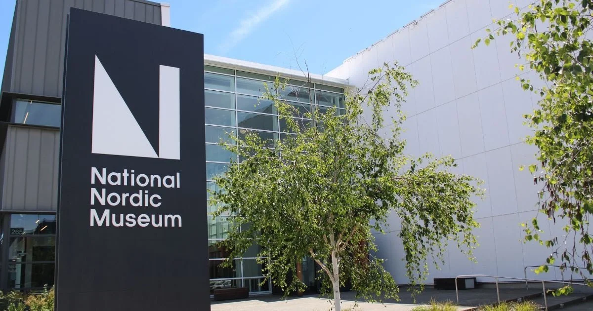 Exterior view of the National Nordic Museum with a large black sign displaying the museum's name and logo, trees, glass windows, and a white building facade.