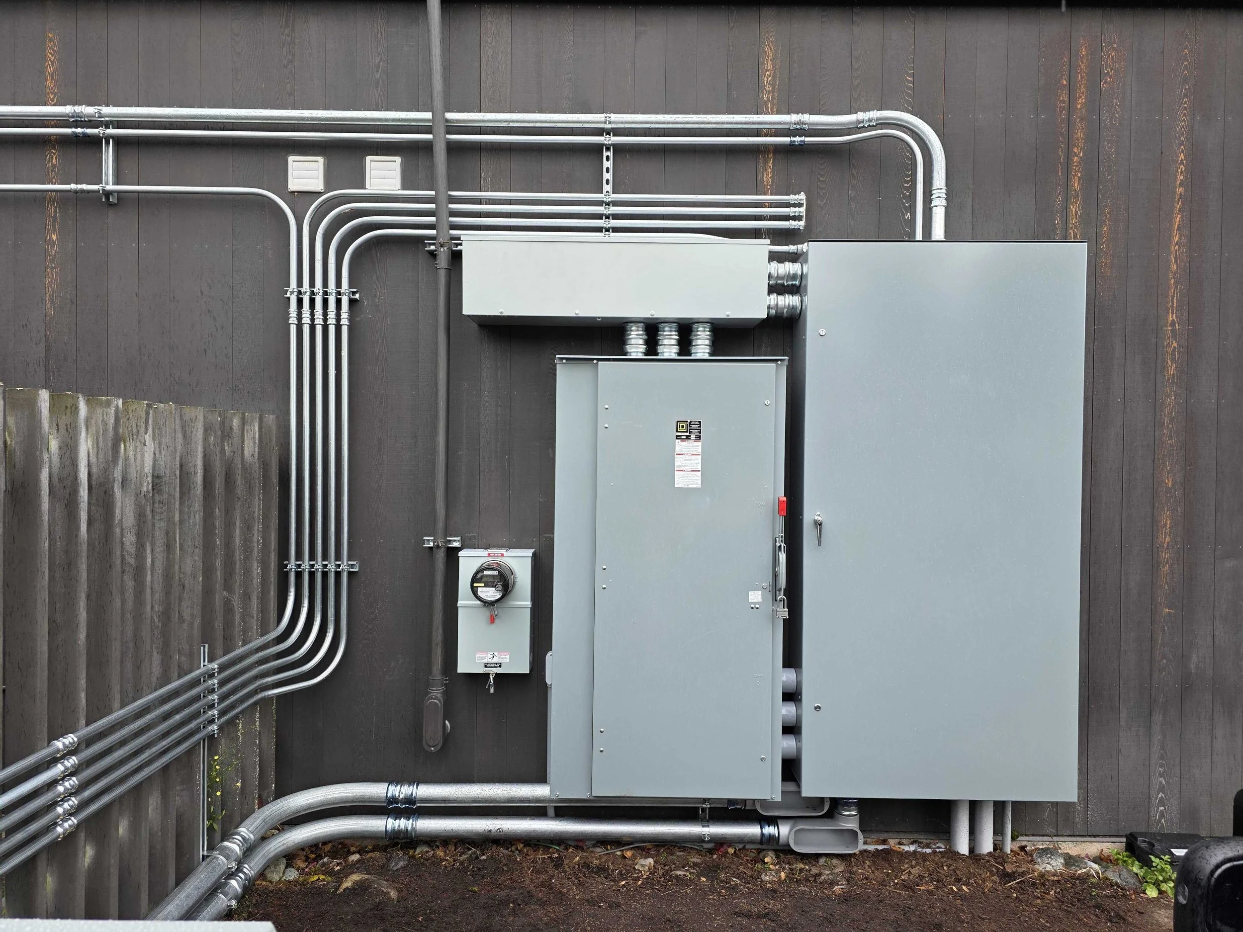 Electrical and communication conduits and boxes mounted on a wooden wall.