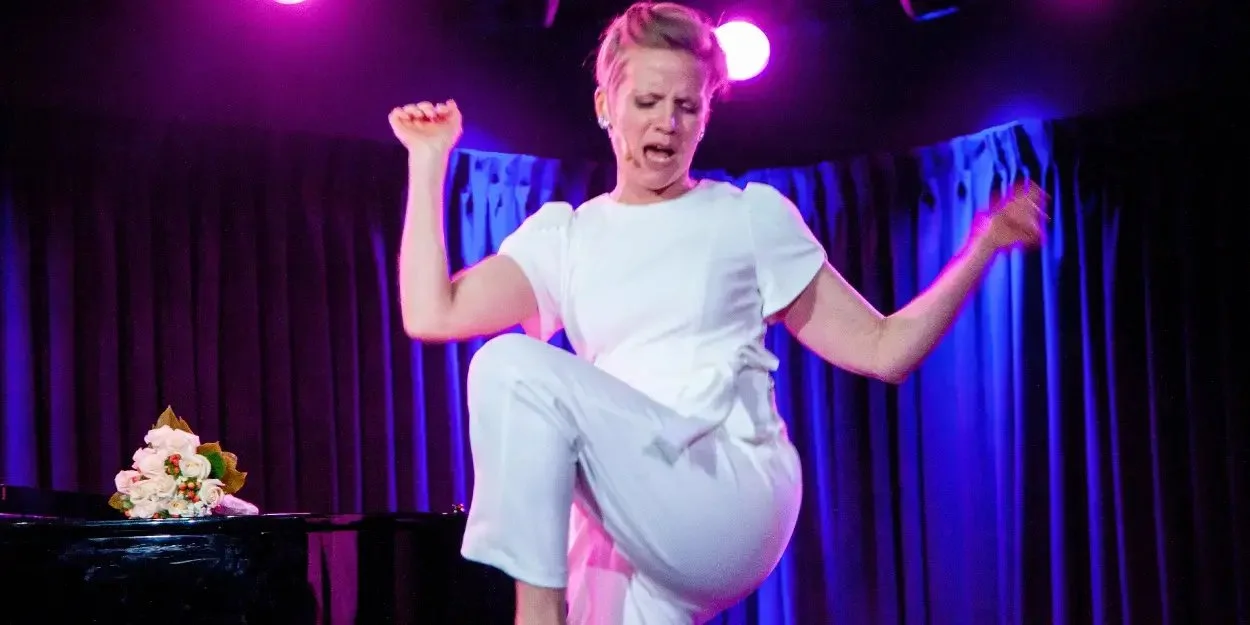 A woman in a white outfit dancing on stage with purple curtains and lighting, and a bouquet of flowers on a piano nearby.