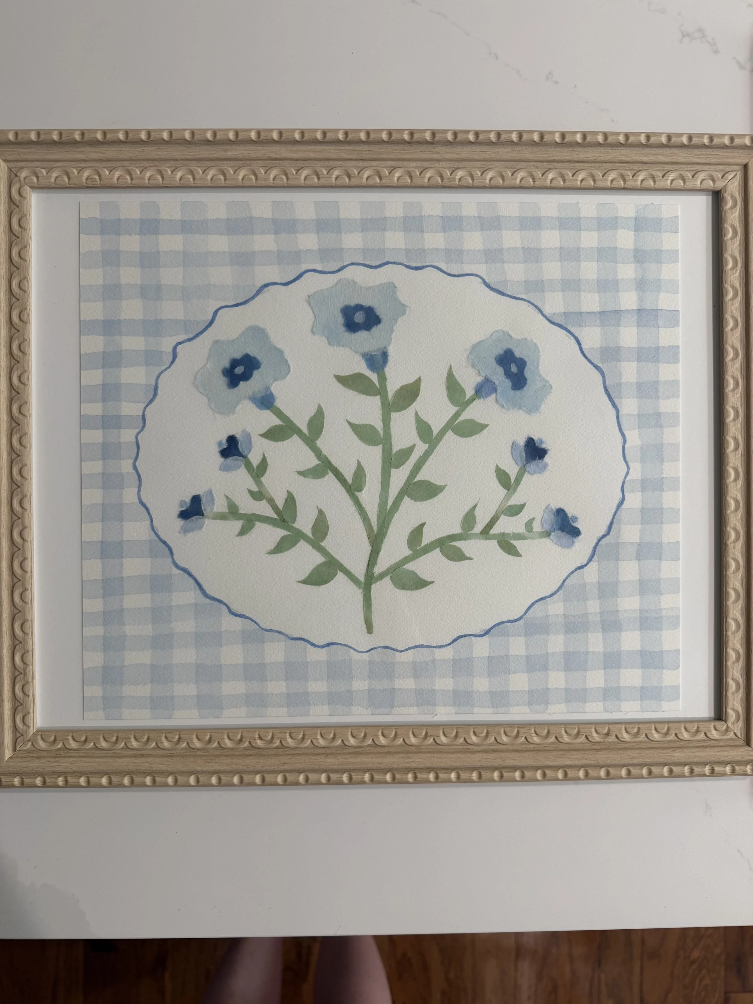 Framed artwork of a blue floral arrangement on a light blue and white checkered background.