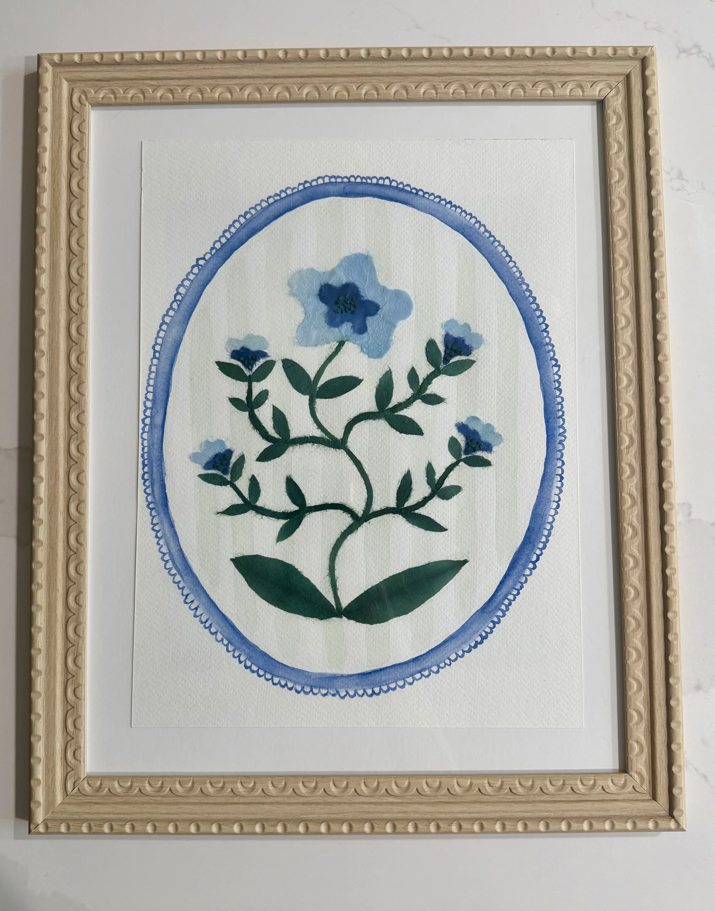 Artwork featuring blue flowers with green stems inside a decorative blue oval frame, mounted in a wooden frame with carved details.