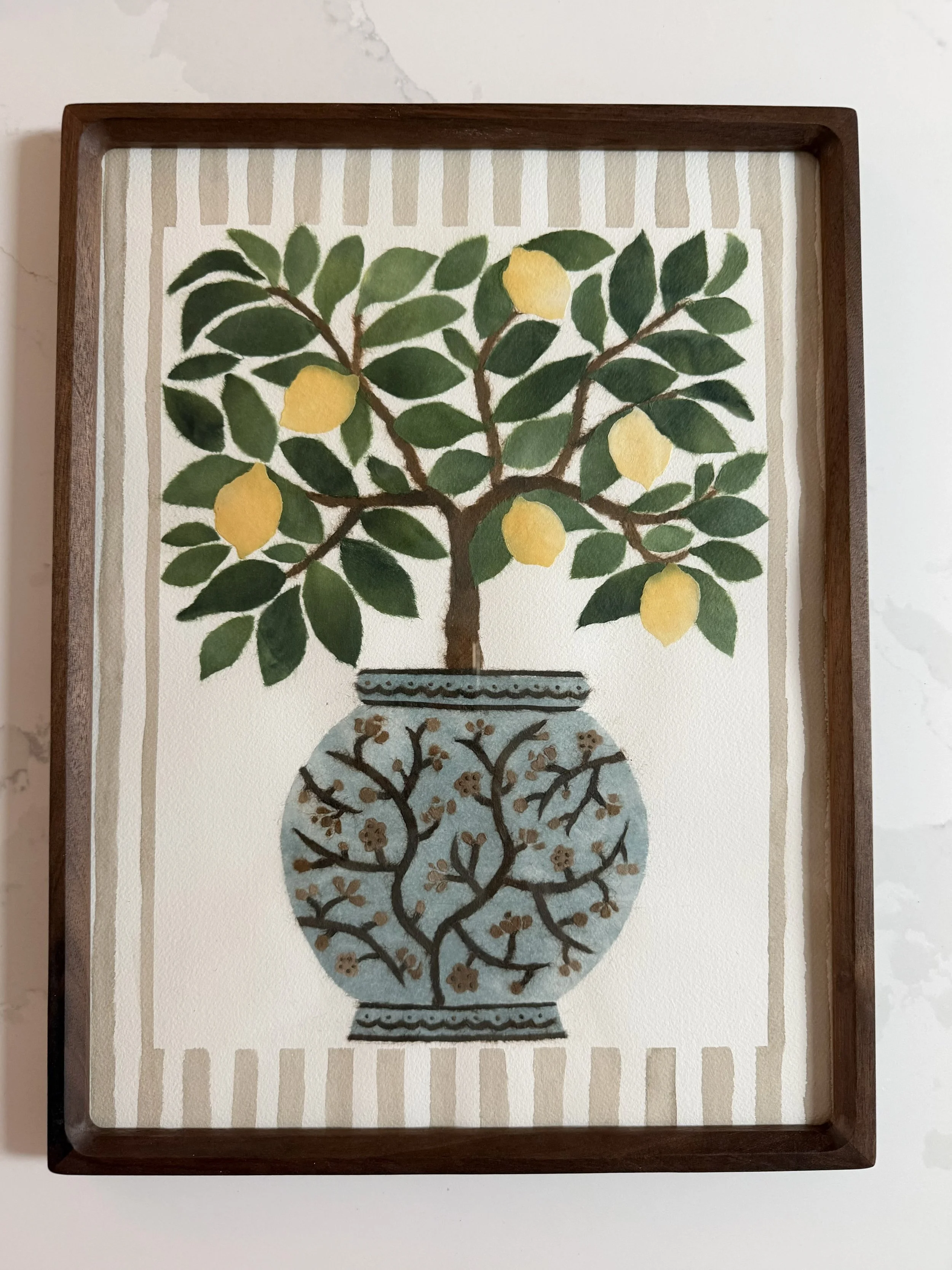 A framed chigiri-e piece of a lemon tree in a decorative vase with lemon fruits and green leaves, set against a background with brown and white vertical stripes.