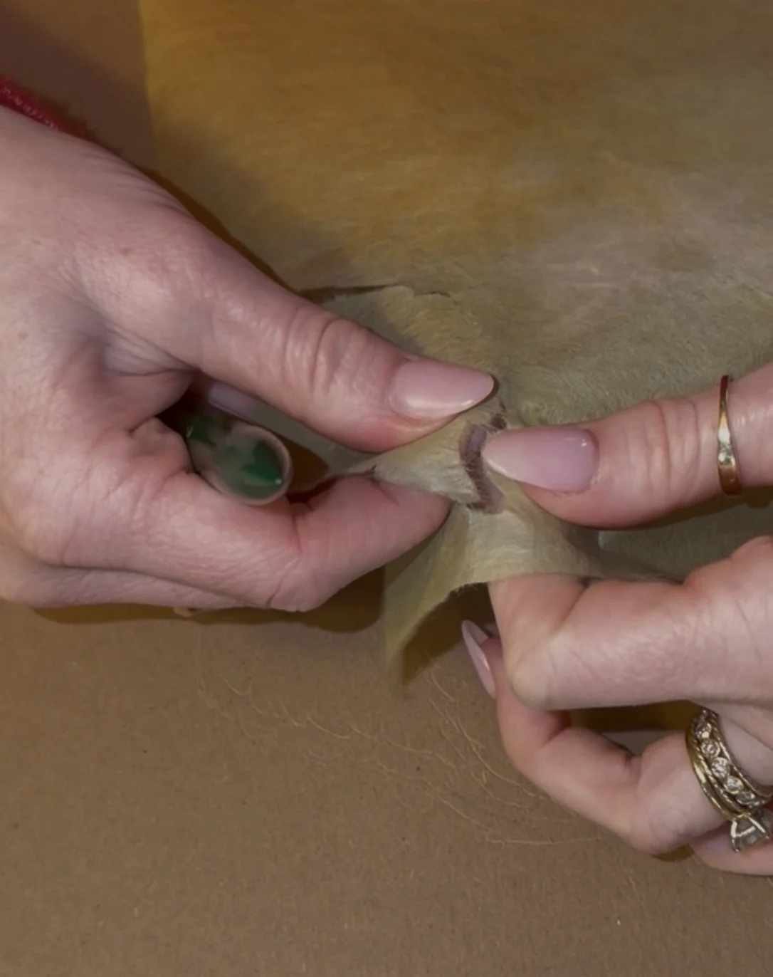 Person's hands tearing a piece a leaf out of green washi paper on top of a brown surface.