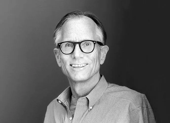 Black and white portrait of a smiling man with glasses in a button-up shirt, facing slightly to the right.
