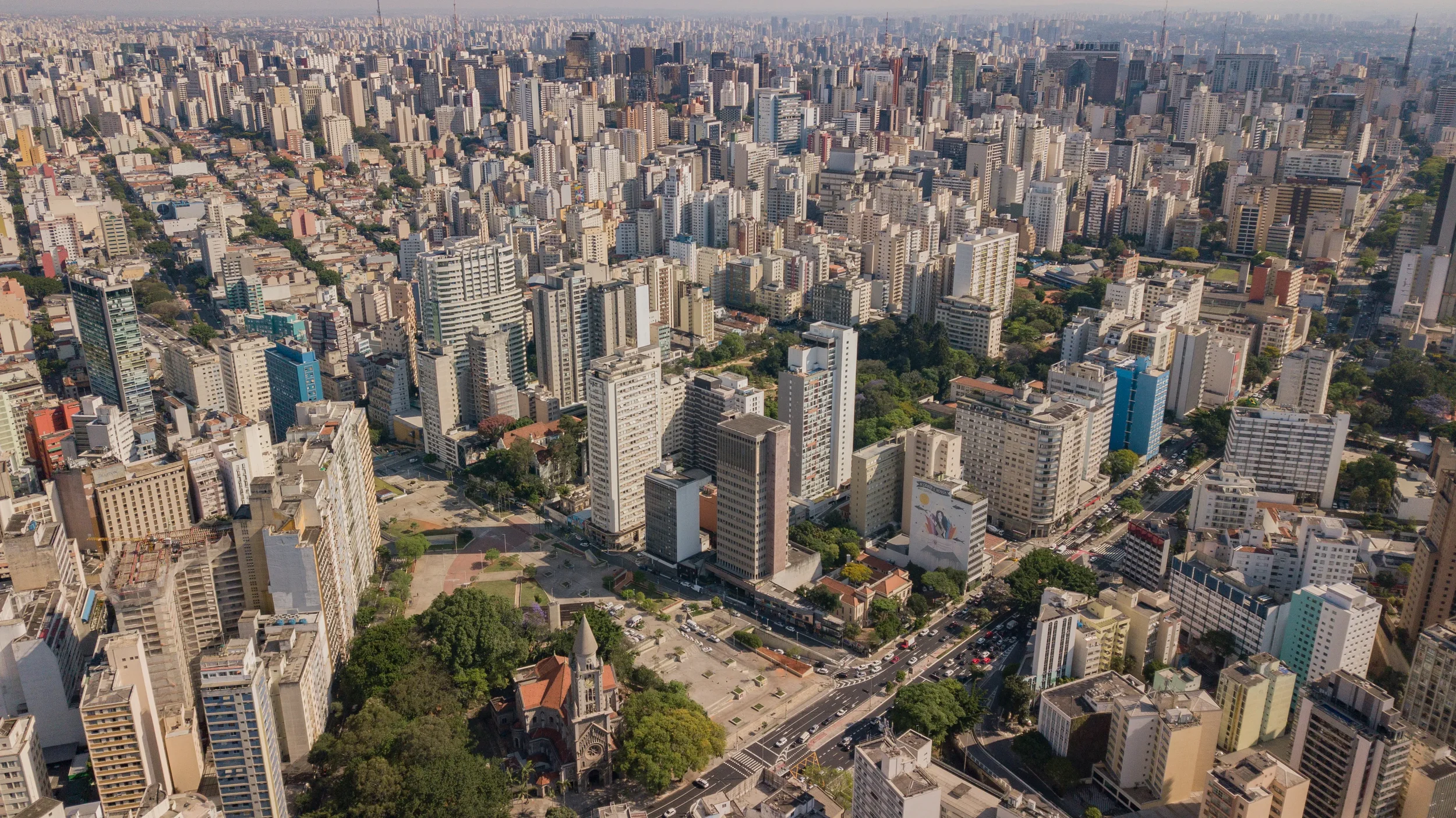 Imagem aérea de uma cidade com muitos prédios altos, ruas e árvores.