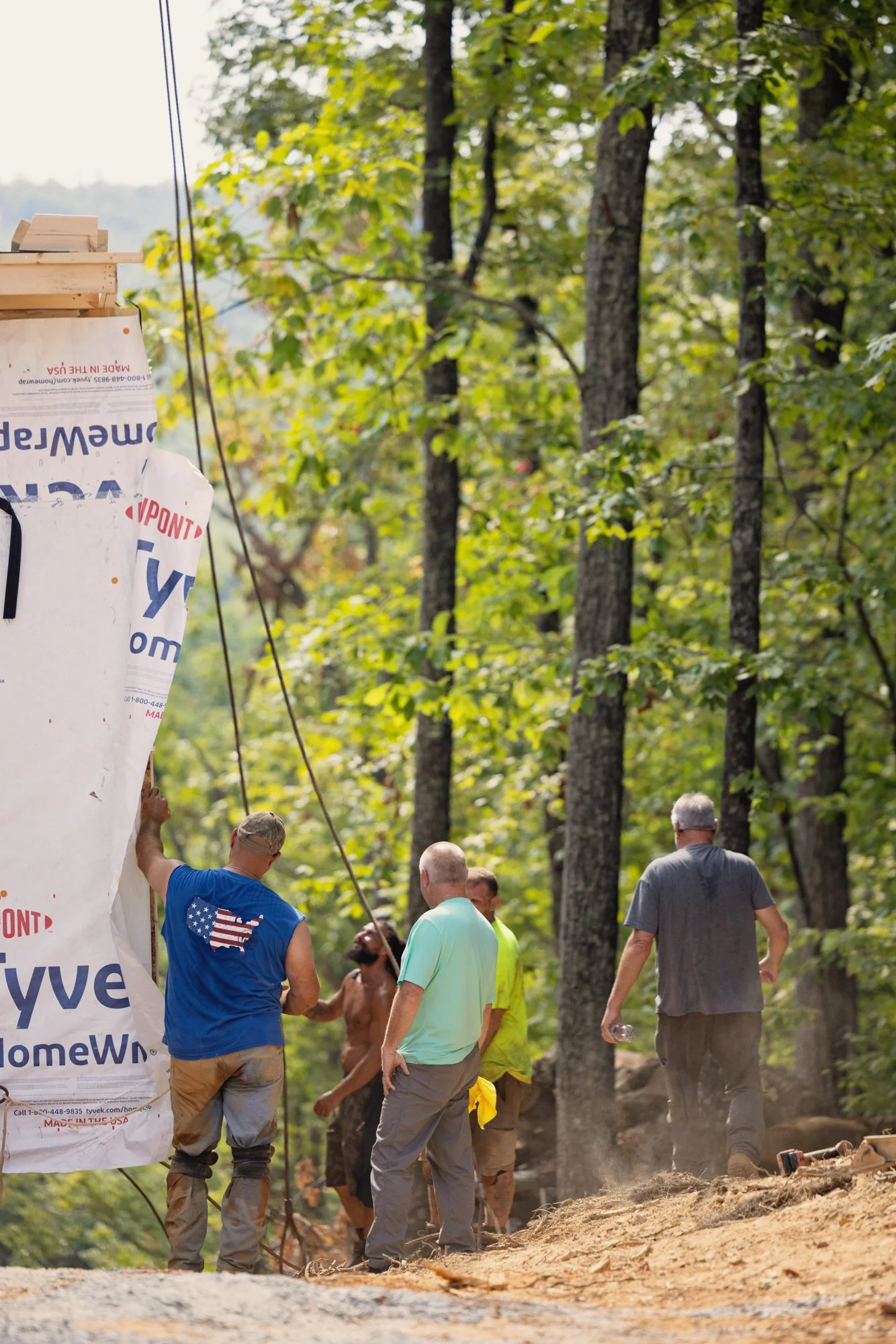 People working on a dirt trail in a forest, with trees and green leaves in the background, and a large banner on the left side of the image.