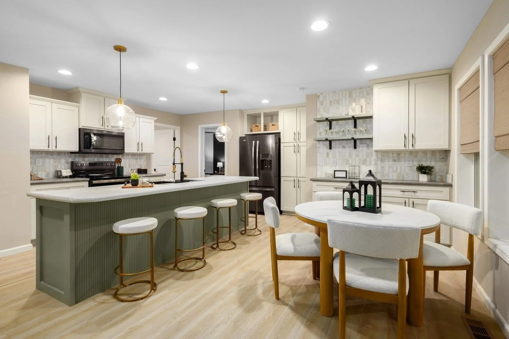 Modern kitchen with white cabinets, marble countertops, black appliances, and a dining area with a round table and white chairs.