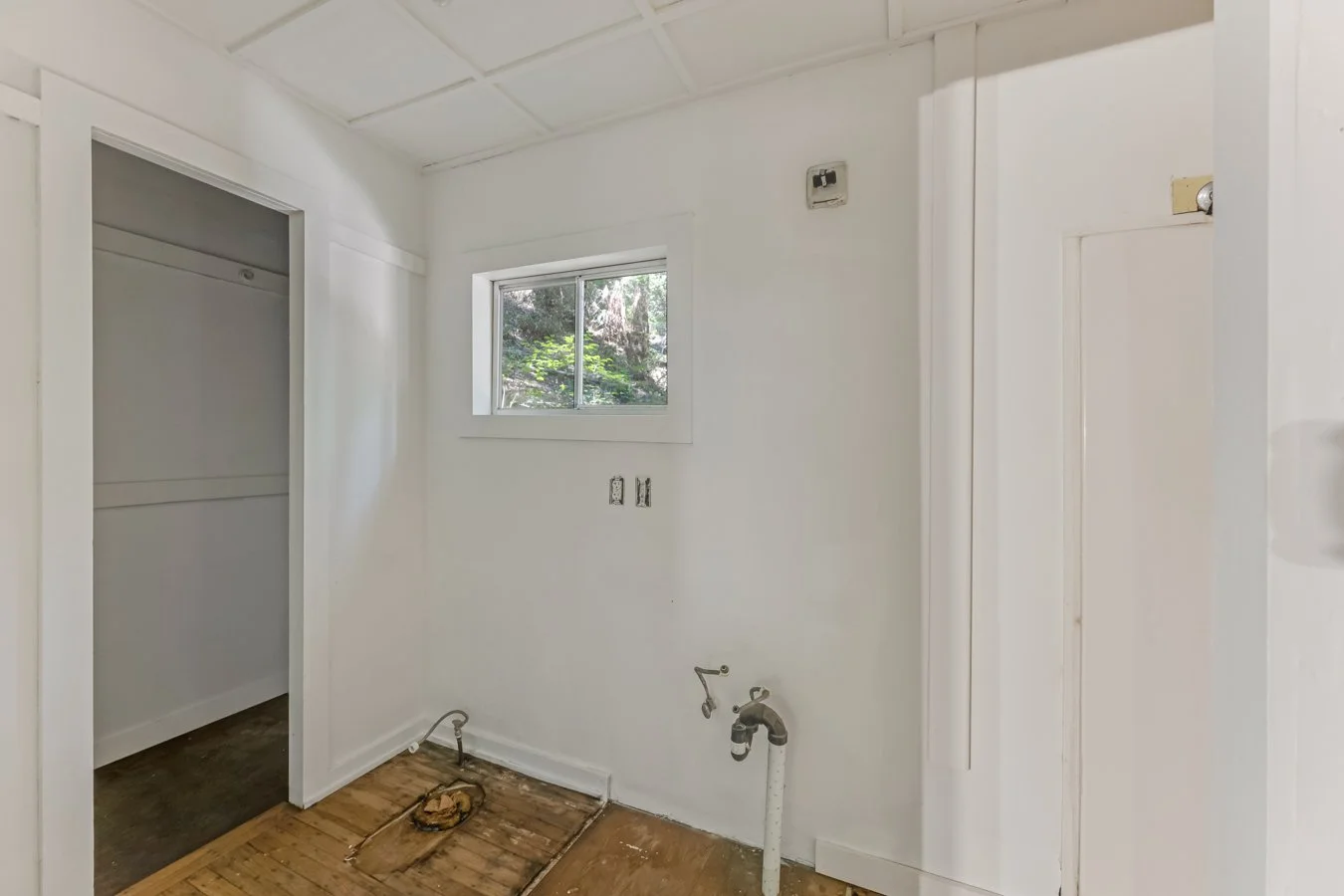 Empty laundry room with white walls, a window, and exposed plumbing for a washer and dryer.