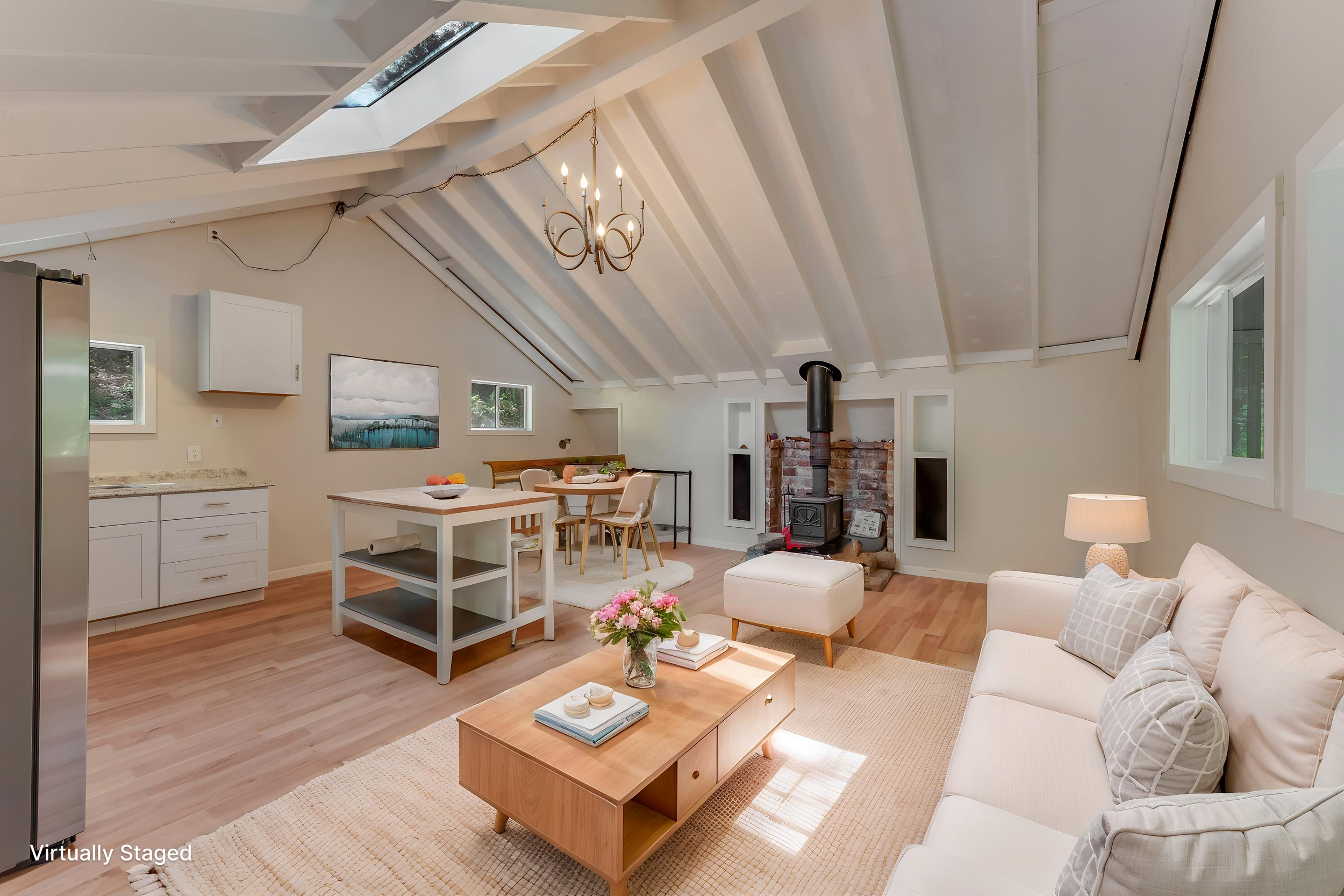 Living room with vaulted ceiling, skylight, chandelier, brick fireplace, television, windows, white couch, coffee table, and decorative pillows.