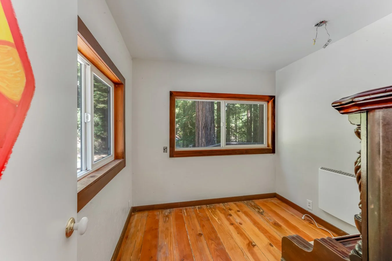 Empty room with white walls, hardwood flooring, two windows with wood trim, and a radiator on the right wall.