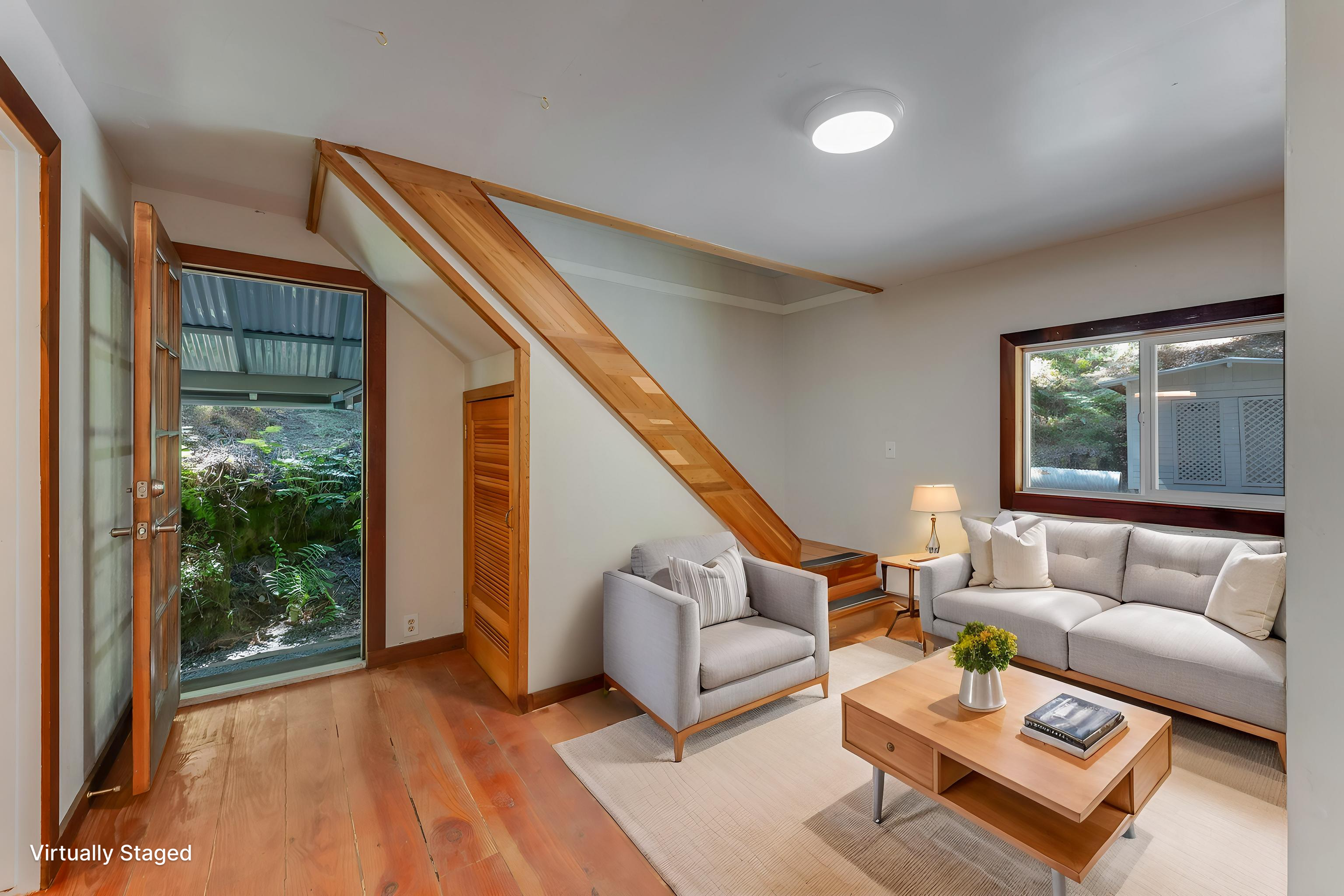 Living room with a beige sofa set, wooden coffee table, window with view of greenery, and front door open to a garden.
