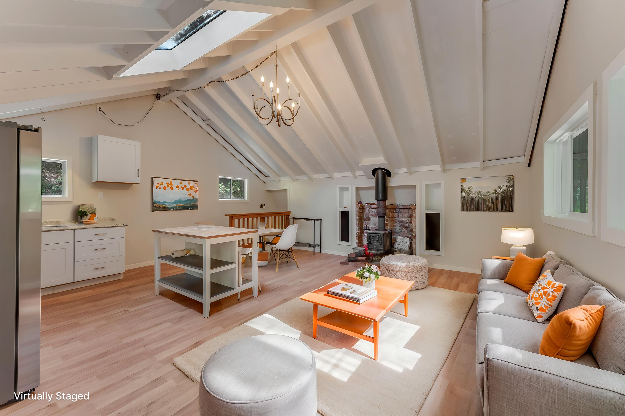 Spacious living room with vaulted ceiling, skylight, modern furniture, artwork, wood stove, and large windows.