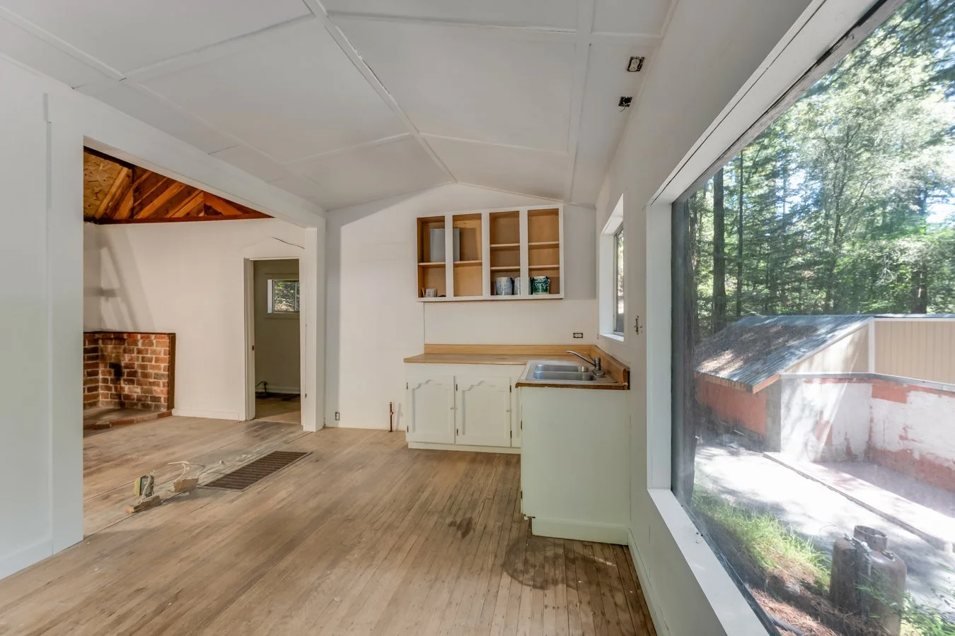 Empty kitchen with white cabinets, open shelves, a small sink, and a large window showing trees outside.