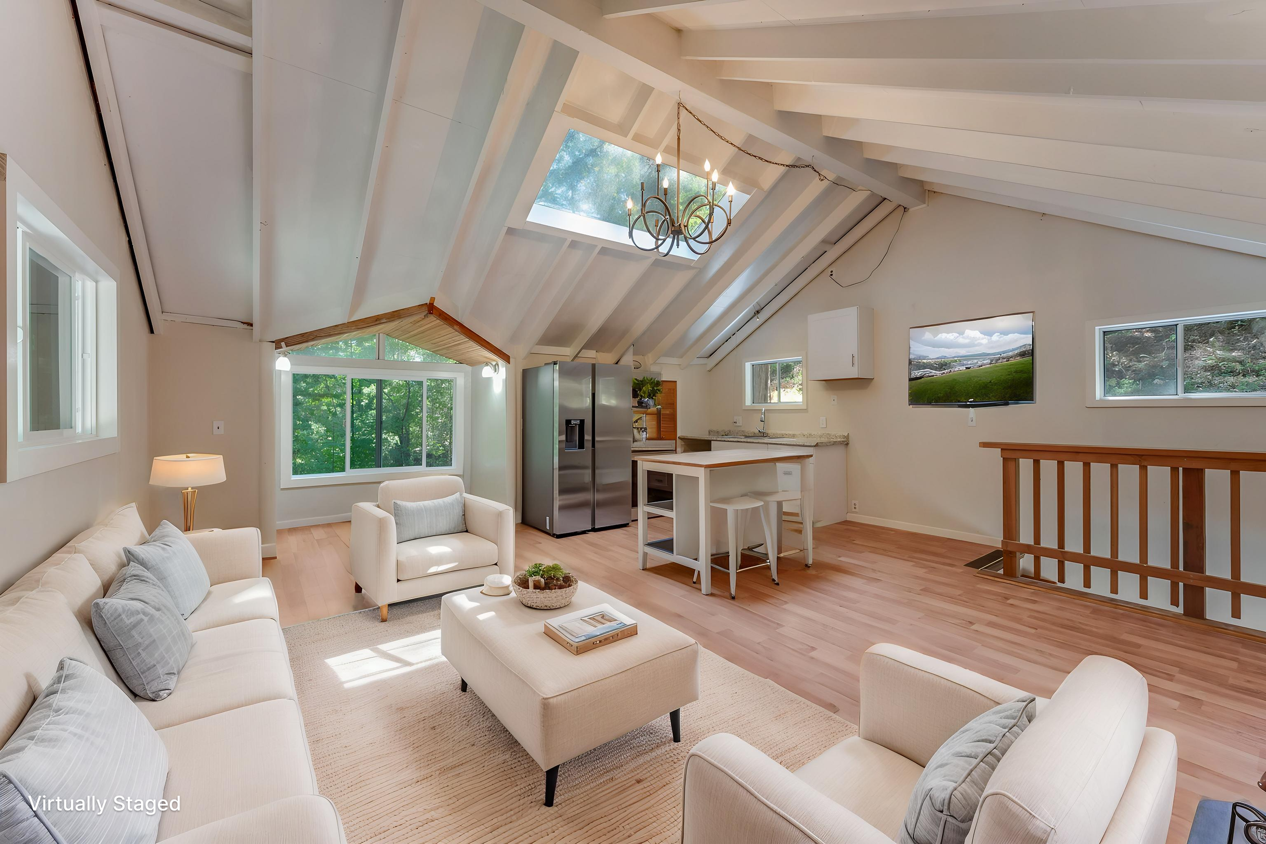 Living room with white sofas and armchairs, a beige rug, a small coffee table, large windows, and a vaulted ceiling with skylights and a chandelier.