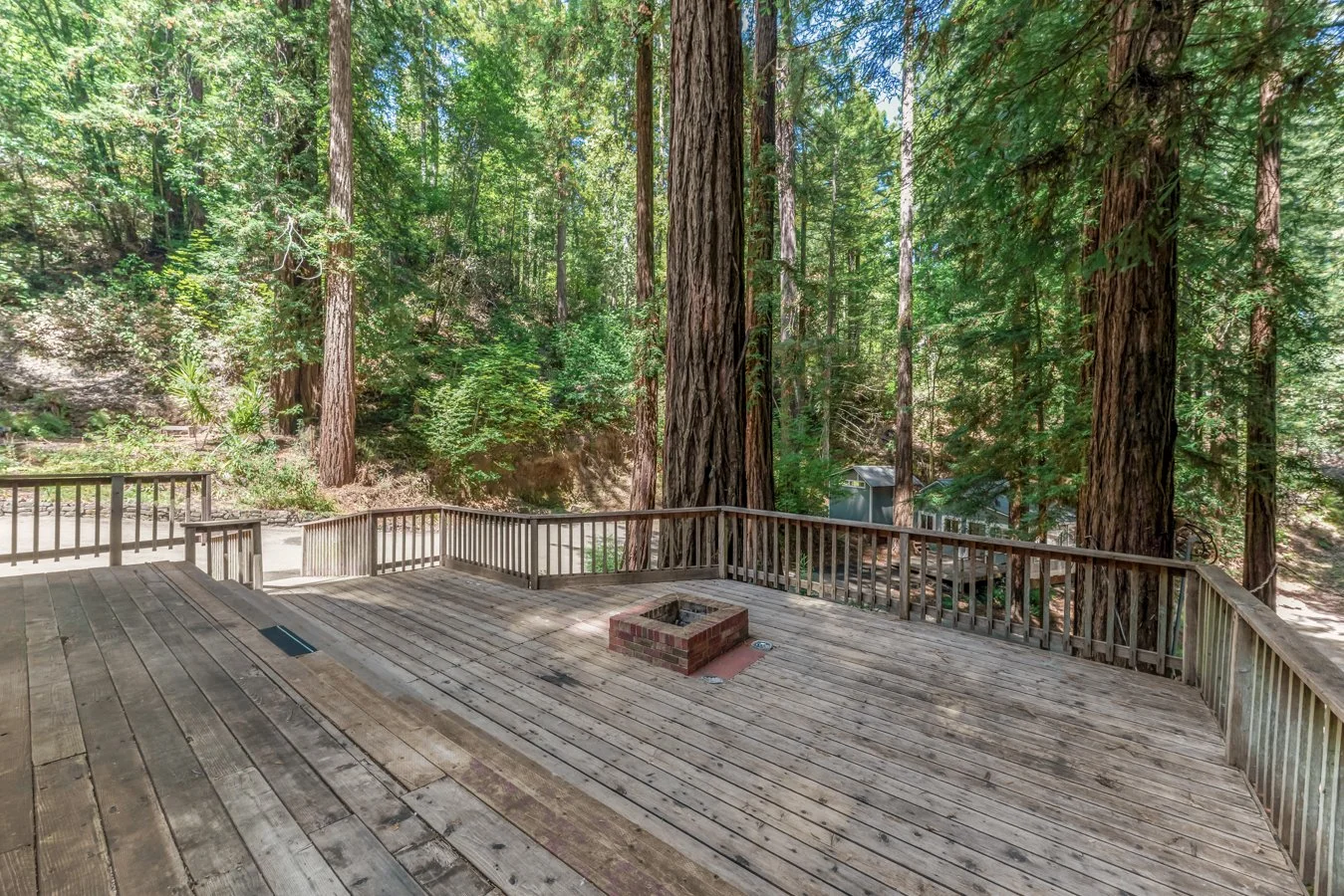 A spacious wooden deck surrounded by tall redwood trees in a forested area.