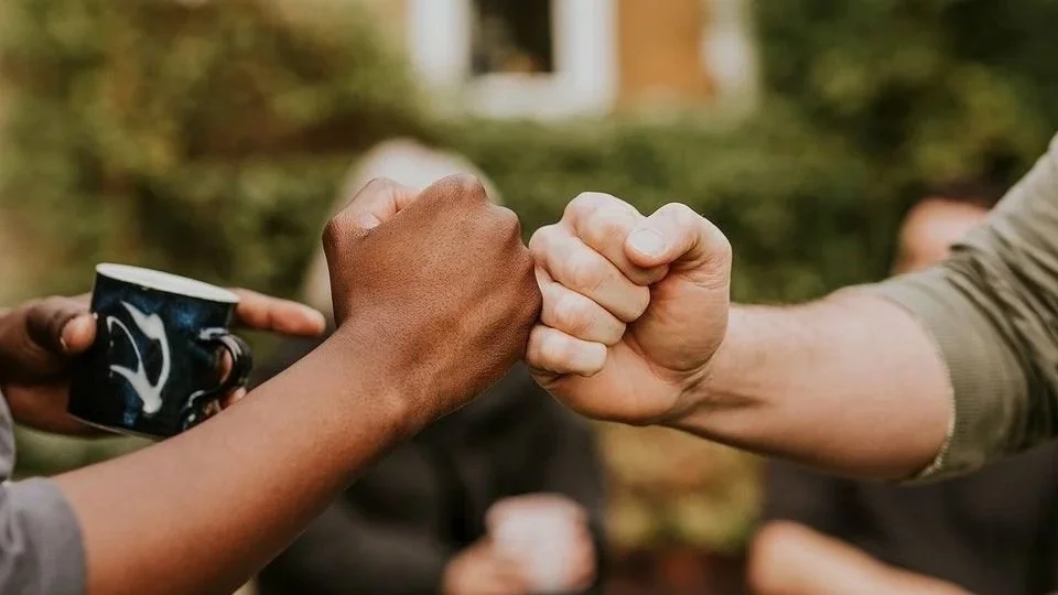 Two people fist bumping outdoors, one holding a coffee cup.