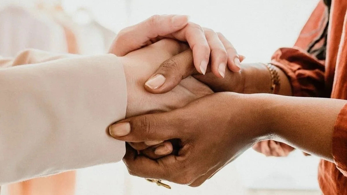 Two people holding hands, one with light skin wearing a white sleeve, and the other with dark skin wearing an orange sleeve.