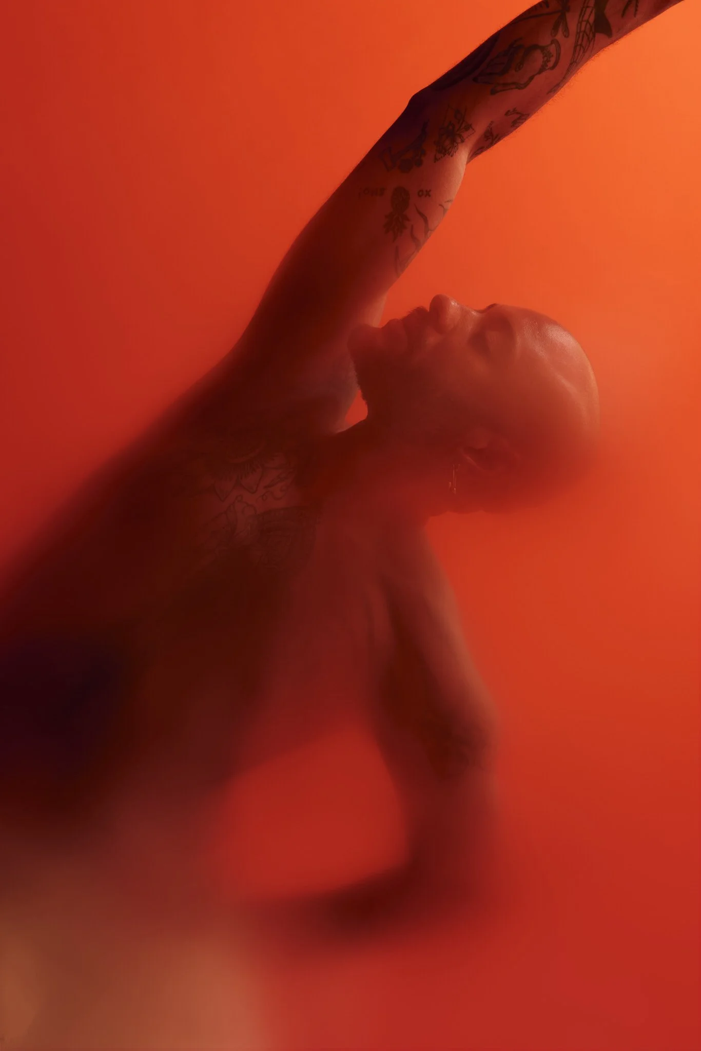 Close-up of a tattooed person dancing or posing in dramatic red-orange lighting.