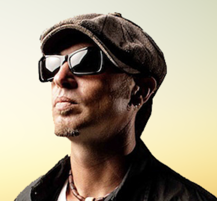 A man wearing a brown cap, black sunglasses, and a black jacket, looking confidently to the side with a light gradient background.