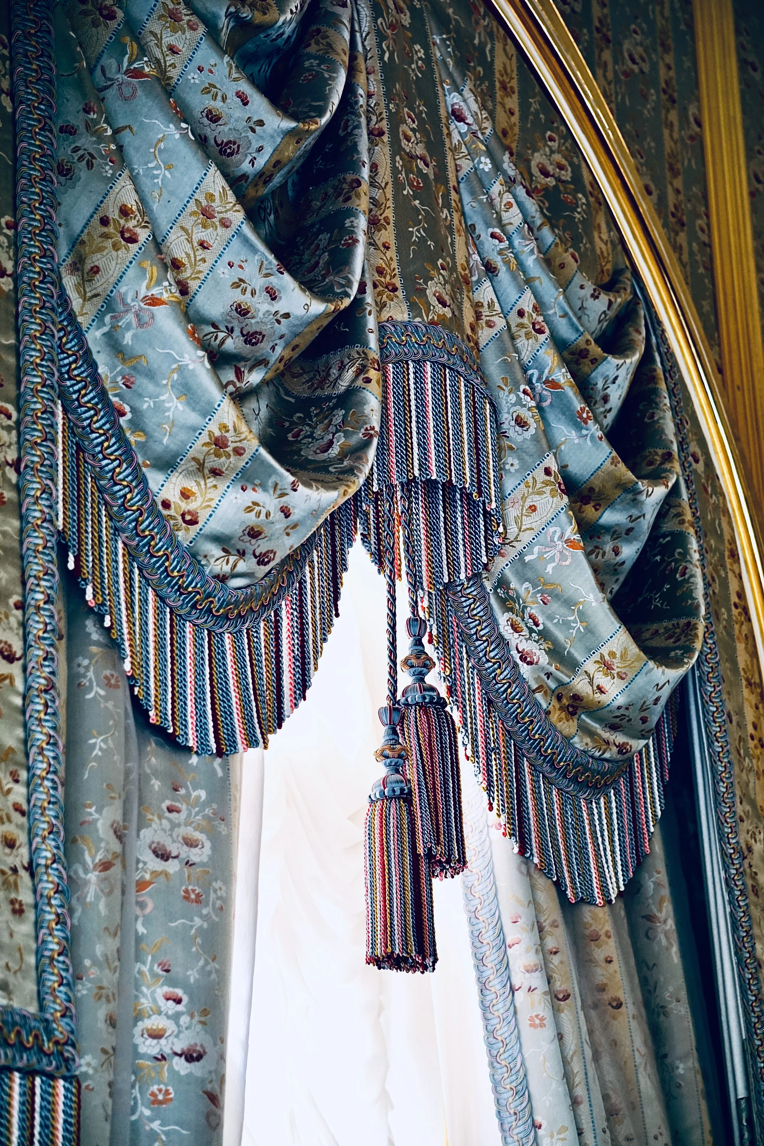 Close-up of ornate fabric with floral and striped patterns, and beaded fringes on a decorated curtain or textile.