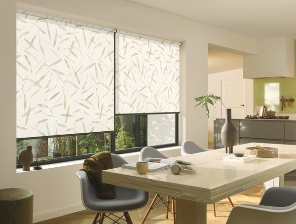 Modern dining room with large window covered by patterned roller shades, a marble table, and contemporary chairs. Kitchen visible in background.