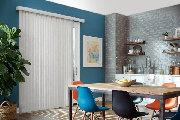 Kitchen and dining area with sliding glass door, colorful chairs, a wooden table, wall art, floating shelves, and a tiled backsplash.