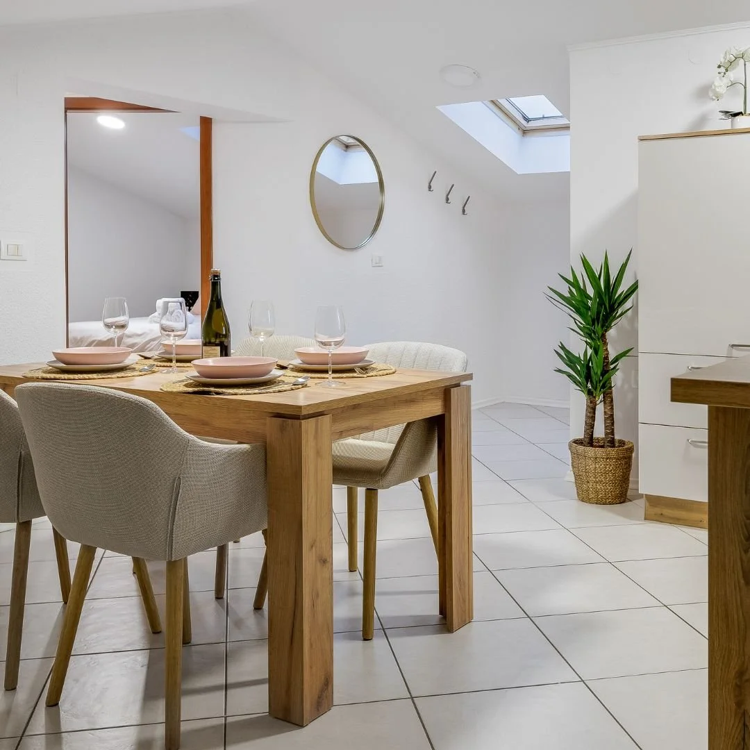 Moderner Essbereich mit Holztisch, vier Stühlen, Weinglas, Weinflasche, Pflanzen, Wandspiegel, Dachfenster und weißer Wand.