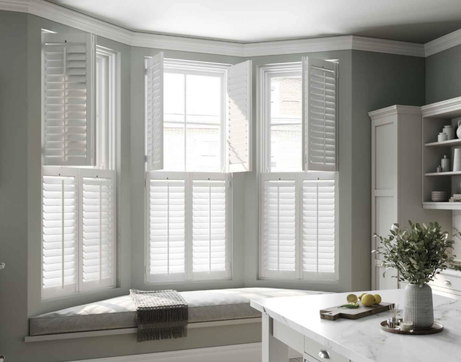 A bright kitchen corner with a window seat, white plantation shutters, and a vase of greenery on the white kitchen island.