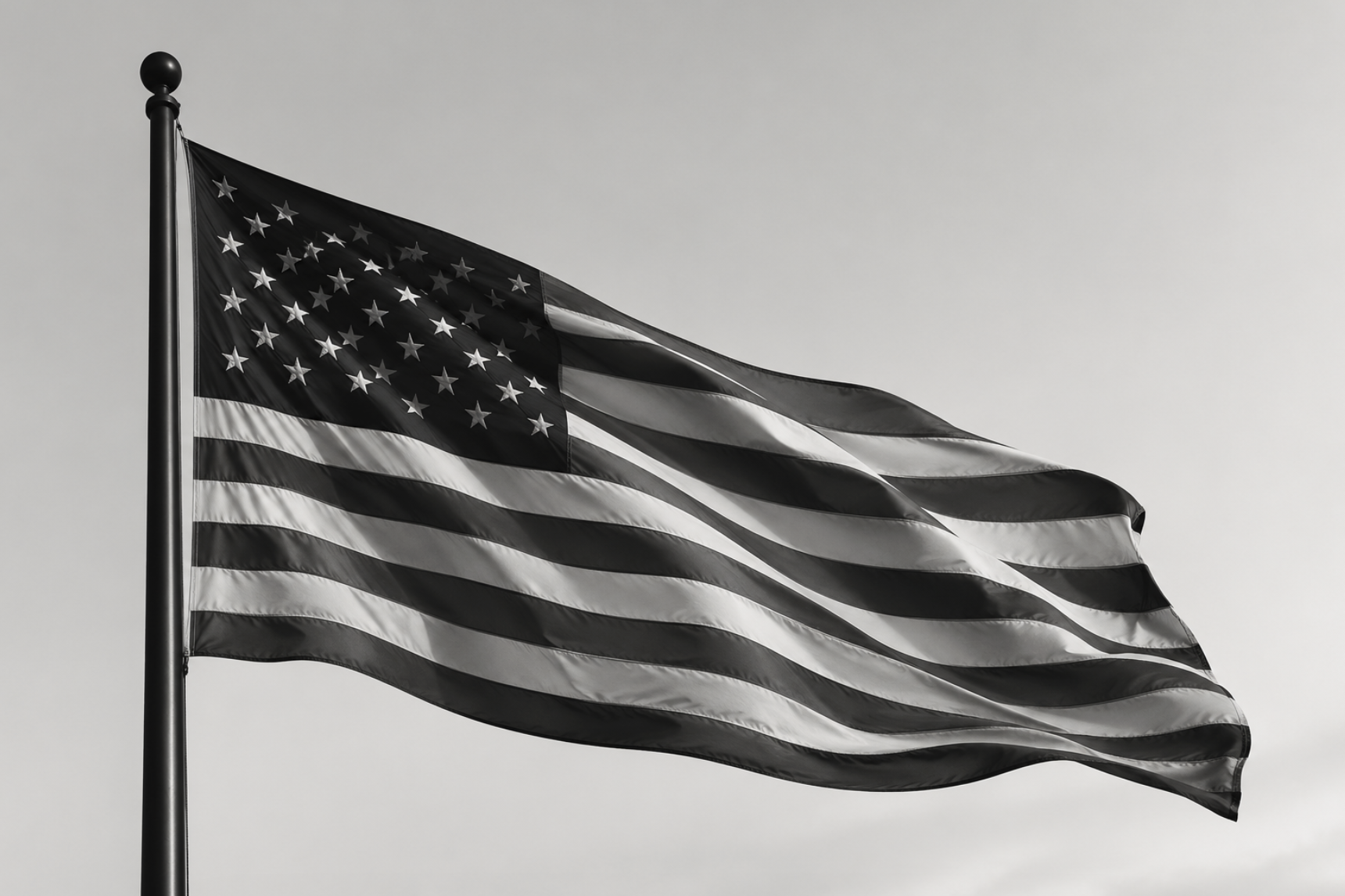 Black and white American flag waving in the wind against a gray sky.