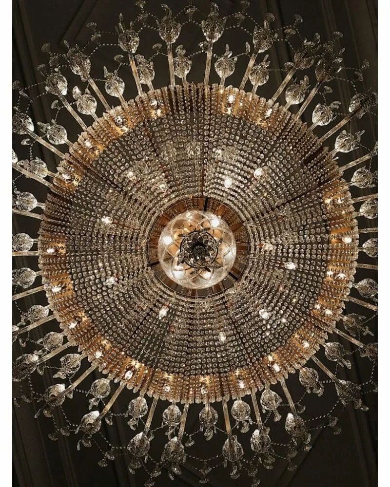 A large, ornate crystal chandelier hanging from a ceiling, with many dangling crystals and lights arranged in a circular pattern.